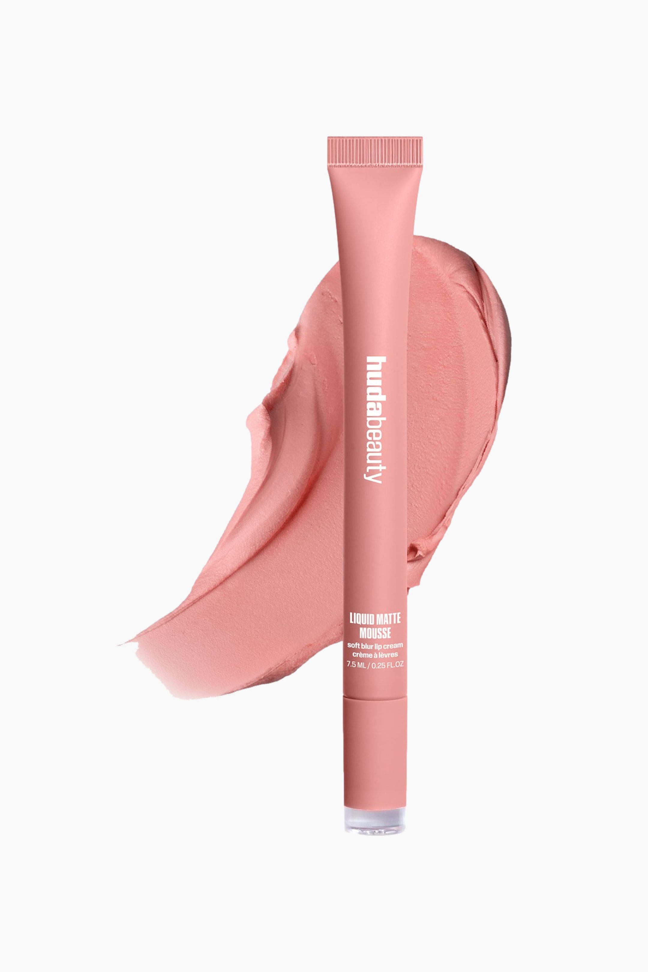Visa större bild: Ett Huda Beauty Liquid Matte Mousse-rör i en matt persikorosa nyans står upprätt och lätt vinklat. Det visar “hudabeauty” vertikalt och produktdetaljer horisontellt, med ett matchande persikorosa krämigt produktprov synligt bakom.