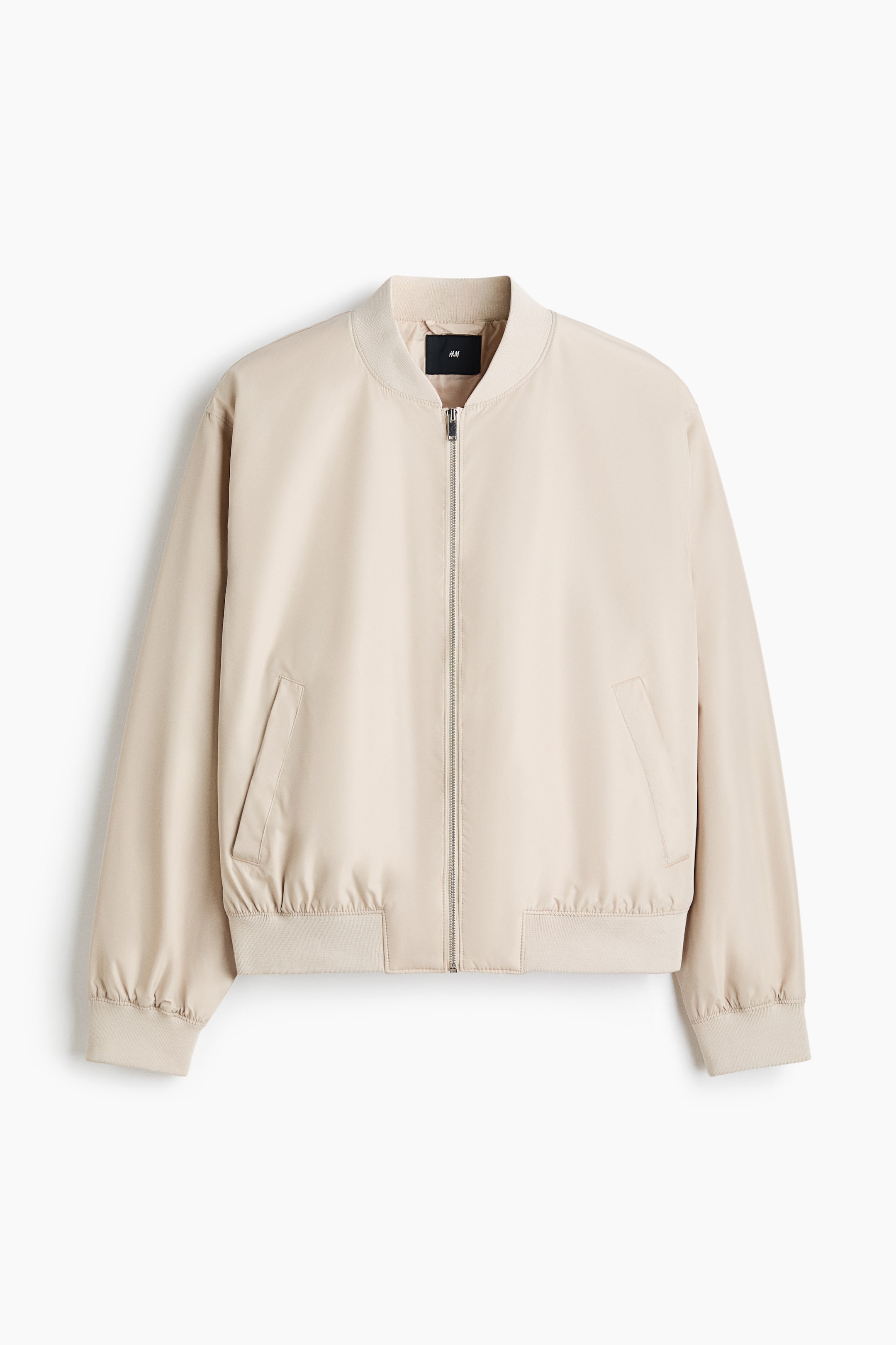 View larger image: A light beige bomber jacket is displaying its front, featuring a ribbed stand-up collar, a full-length silver-toned zipper, two angled front pockets, ribbed cuffs, and a ribbed hem.