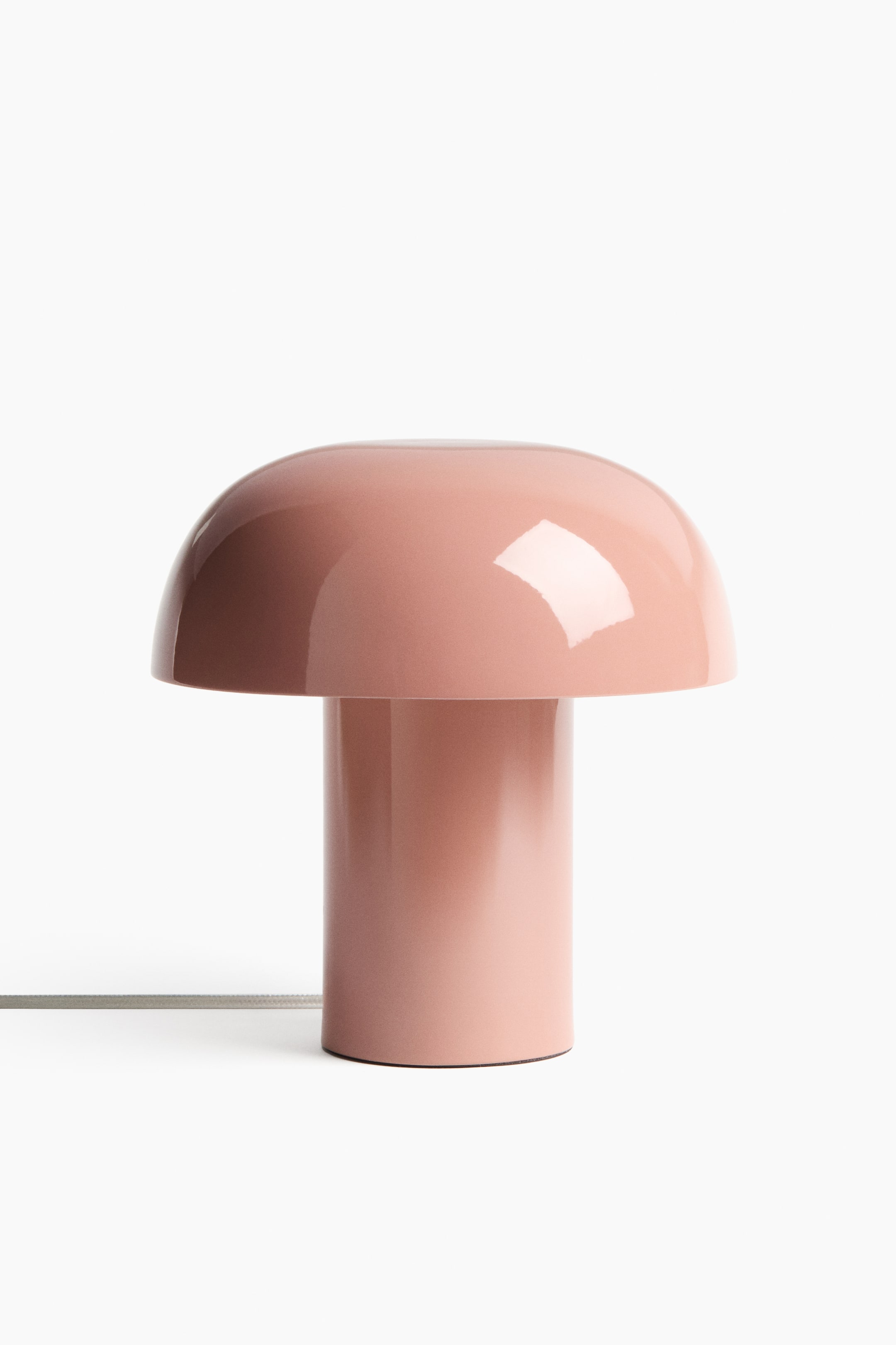 Visa större bild: En modern bordslampa står frontalt och visar upp sin mjuka, svampinspirerade form med en bred, rundad skärm och en cylindrisk bas, båda i en glansig rosa metallfinish. En ljusgrå tygklädd sladd sträcker sig från basen.