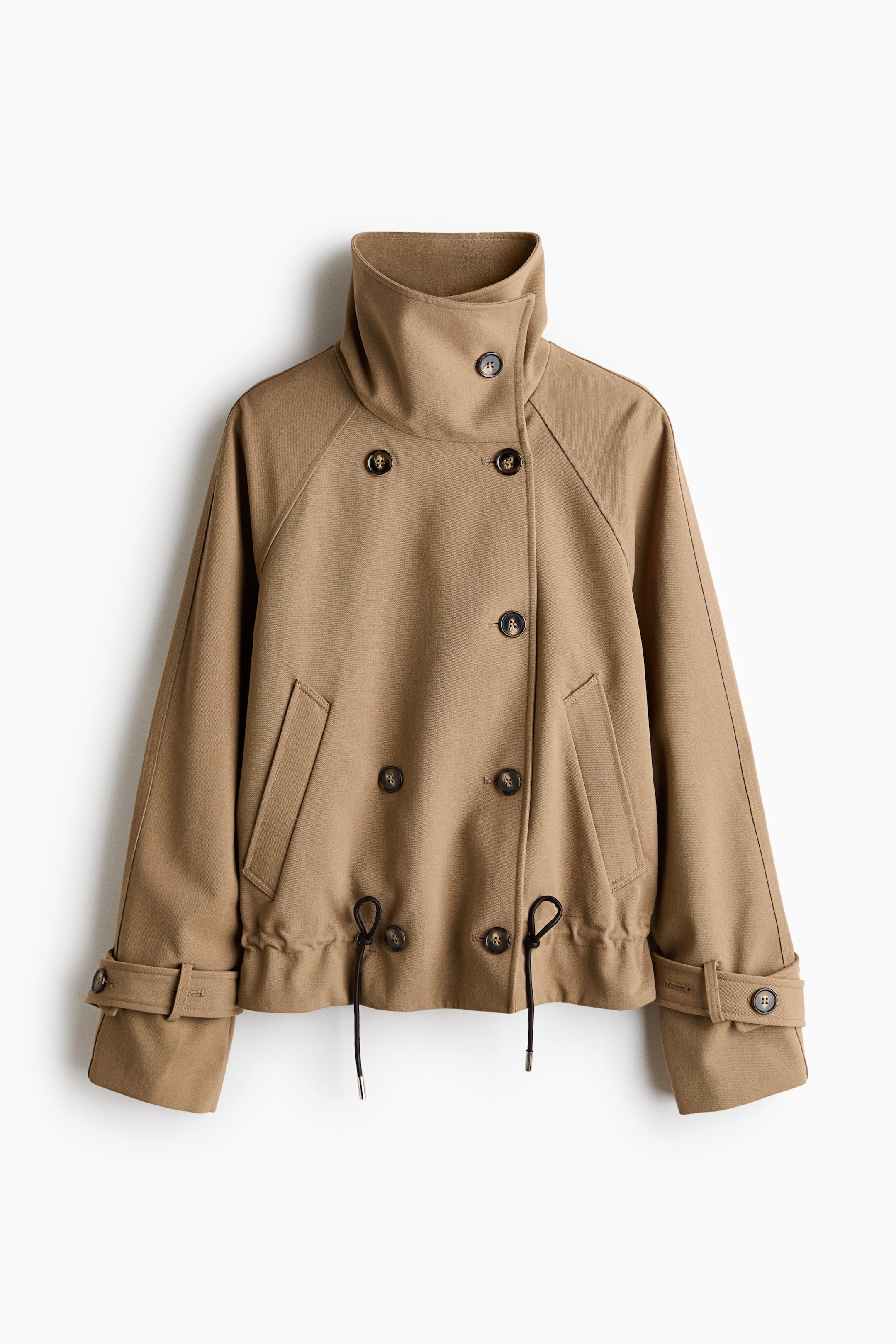 View larger image: A short camel-colored jacket is shown from the front, featuring a high funnel-neck collar and a double-breasted button closure. The jacket features raglan sleeves with buttoned cuff straps, diagonal welt pockets, and a gathered hem with adjustable black drawstrings.