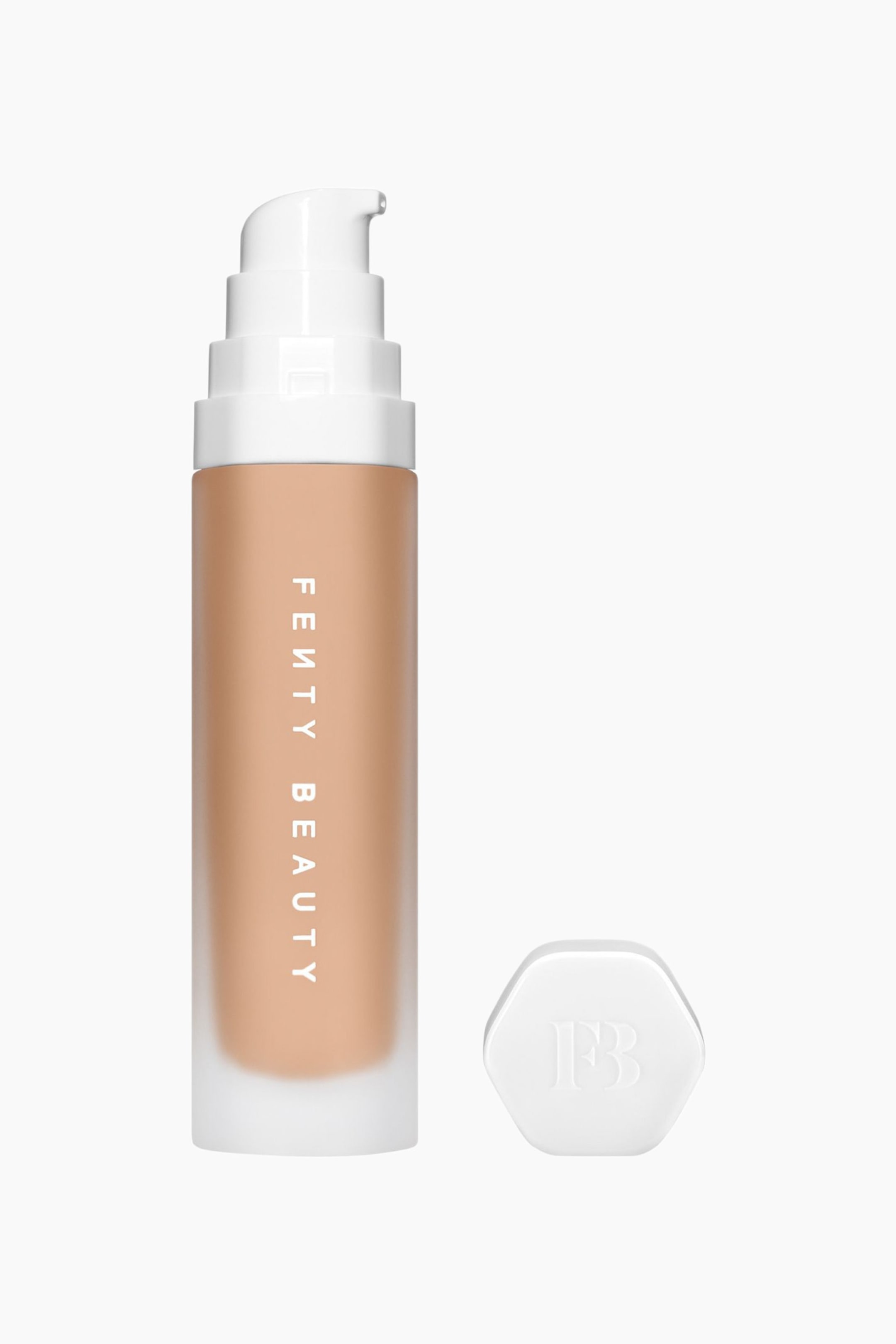 Visa större bild: Soft'lit Naturally Luminous Longwear Foundation står upprätt i en frostad cylindrisk flaska och visar en medium-tan-färgad flytande formula inuti. Den är försedd med en vit, etagerad pumpdispenser på toppen med "FENTY BEAUTY" tryckt vertikalt på framsidan, medan en separat vit sexkantig kork ligger bredvid.