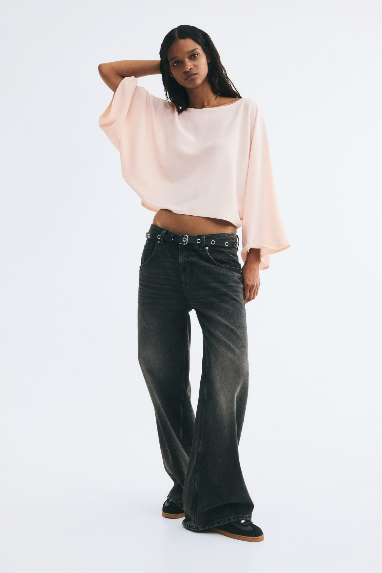 A short, loose-fit knit top in a pale pink shade is hanging front-facing, featuring a wide boat neckline and long, flowing cape sleeves. - 1