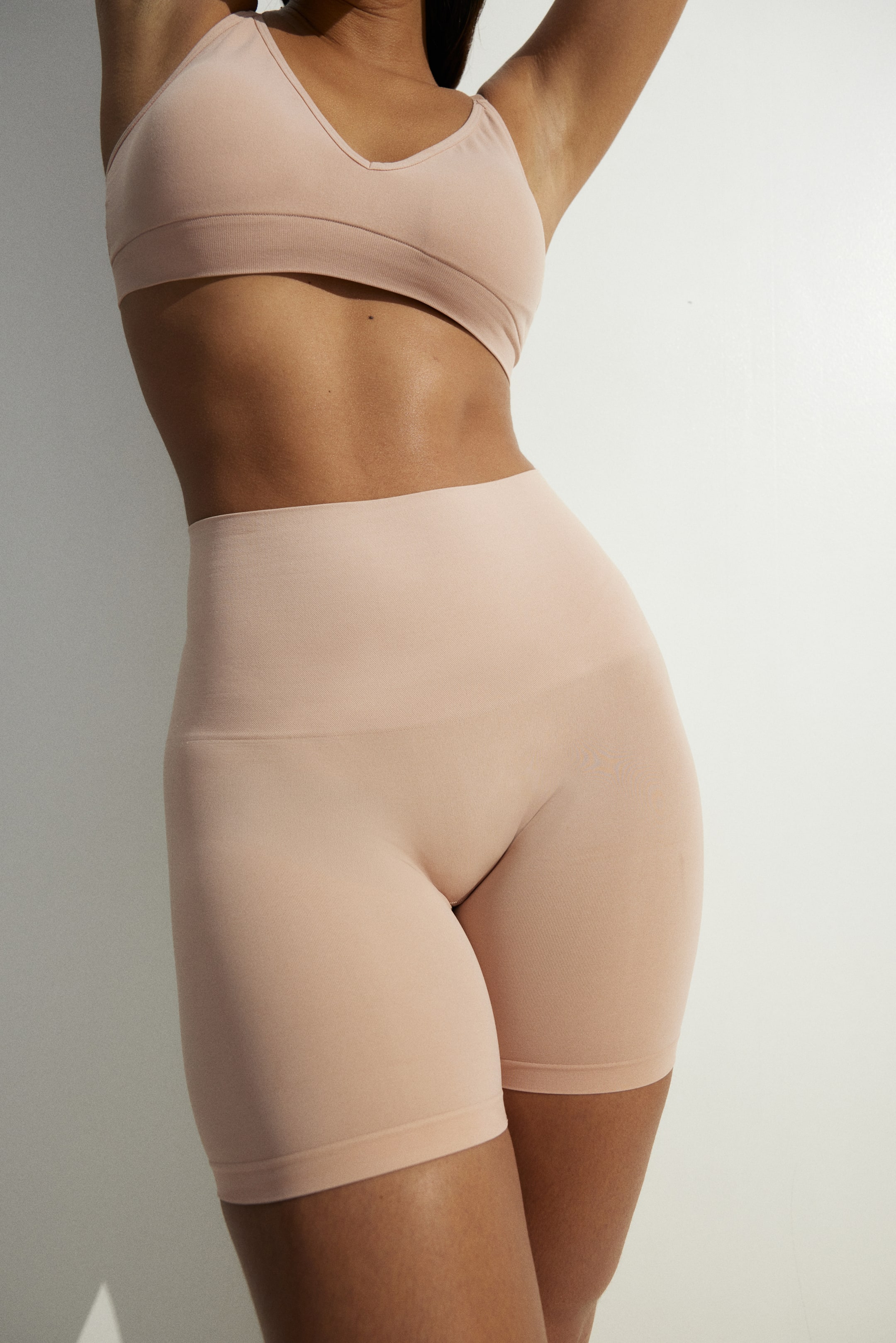 Ver imagen más grande: Un bralette sin costuras de color nude y unos shorts de cintura alta a juego se presentan desde un ángulo lateral-frontal, exhibiendo su diseño ajustado. El bralette cuenta con un escote en V y una banda inferior ancha, mientras que los shorts se extienden hasta la mitad del muslo con una cintura ancha y suavizante.