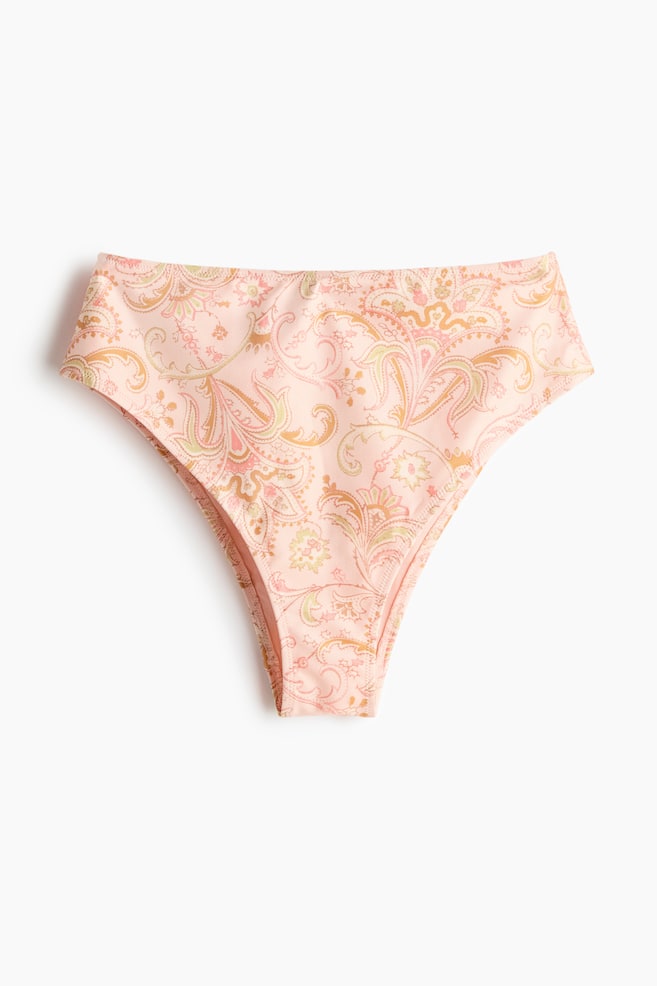 A fully lined bikini bottom is displaying its FRONT, featuring a high waist and a light pink base with an intricate paisley pattern in shades of yellow, orange, and green. It is designed with cutaway coverage at the back. - 1