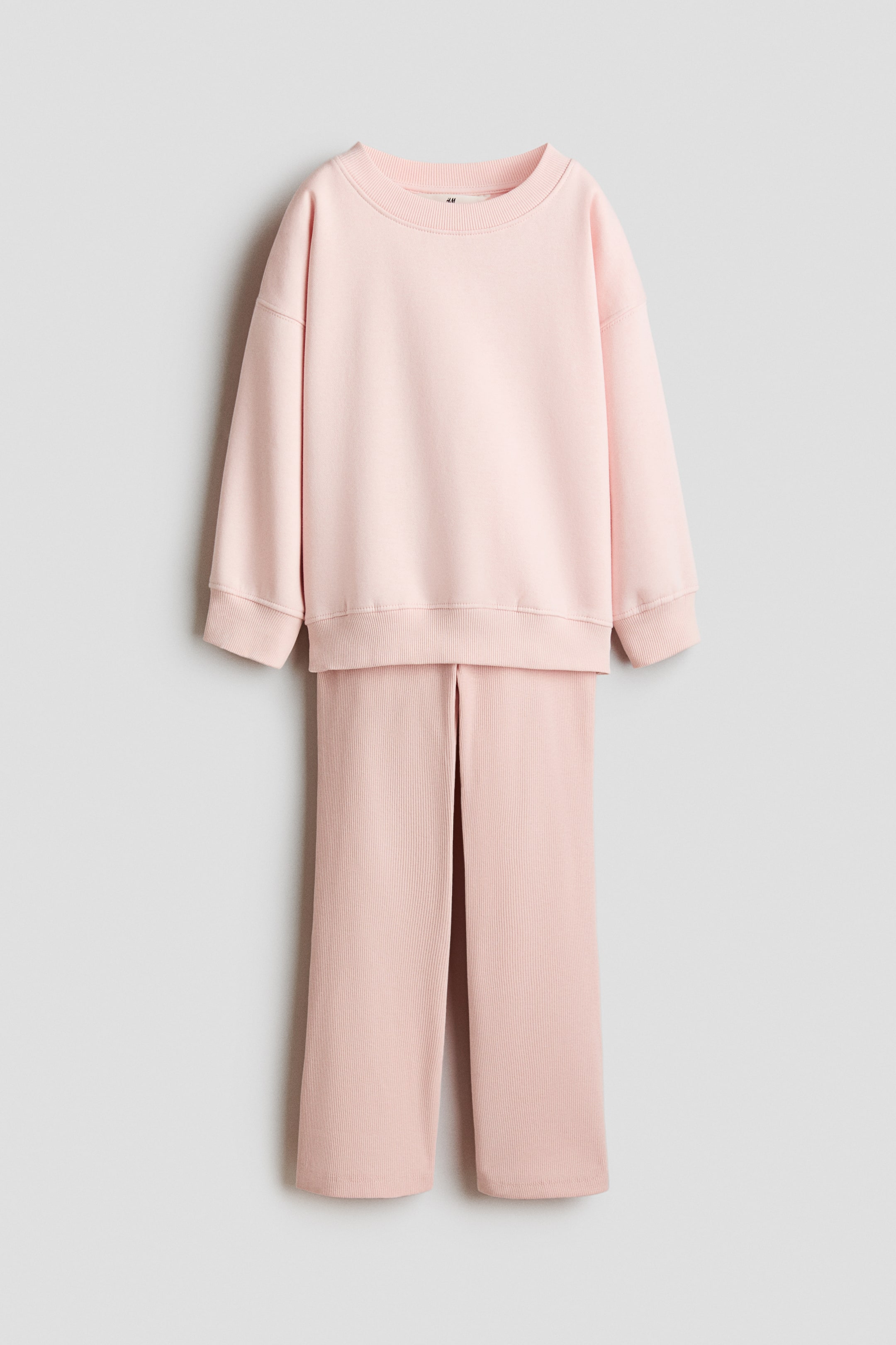 View larger image: A pink two-piece loungewear set is hanging, facing front. It features a smooth, long-sleeved sweatshirt with a ribbed crew neck, ribbed cuffs, and a ribbed hem, paired with ribbed wide-leg pants with front slits on each leg.