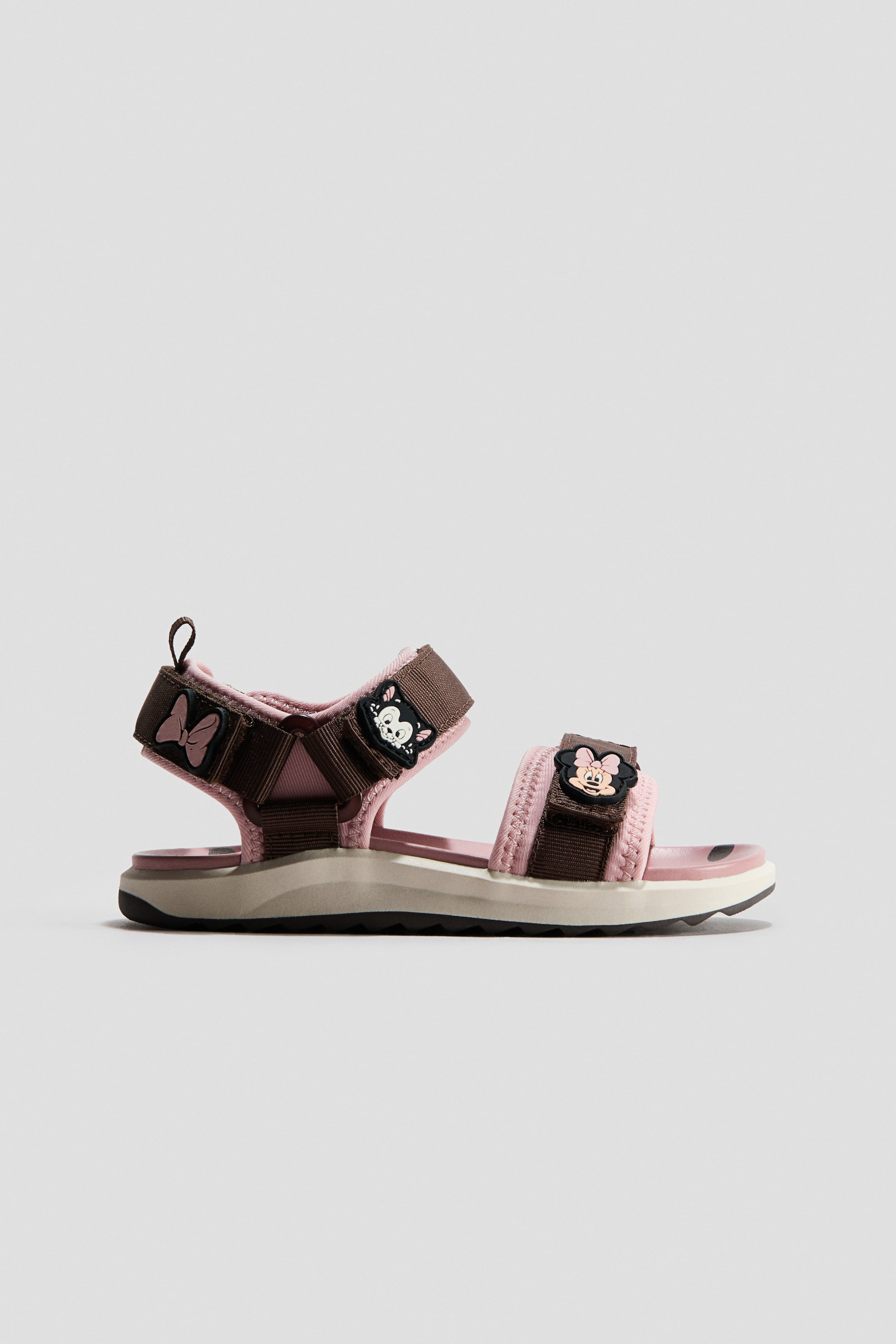 View larger image: A pair of sandals featuring pink padded straps and brown webbing straps, adorned with Minnie Mouse head and bow embellishments. The sandals showcase a multi-layered sole, including a pink footbed, a beige midsole, and a black outsole.