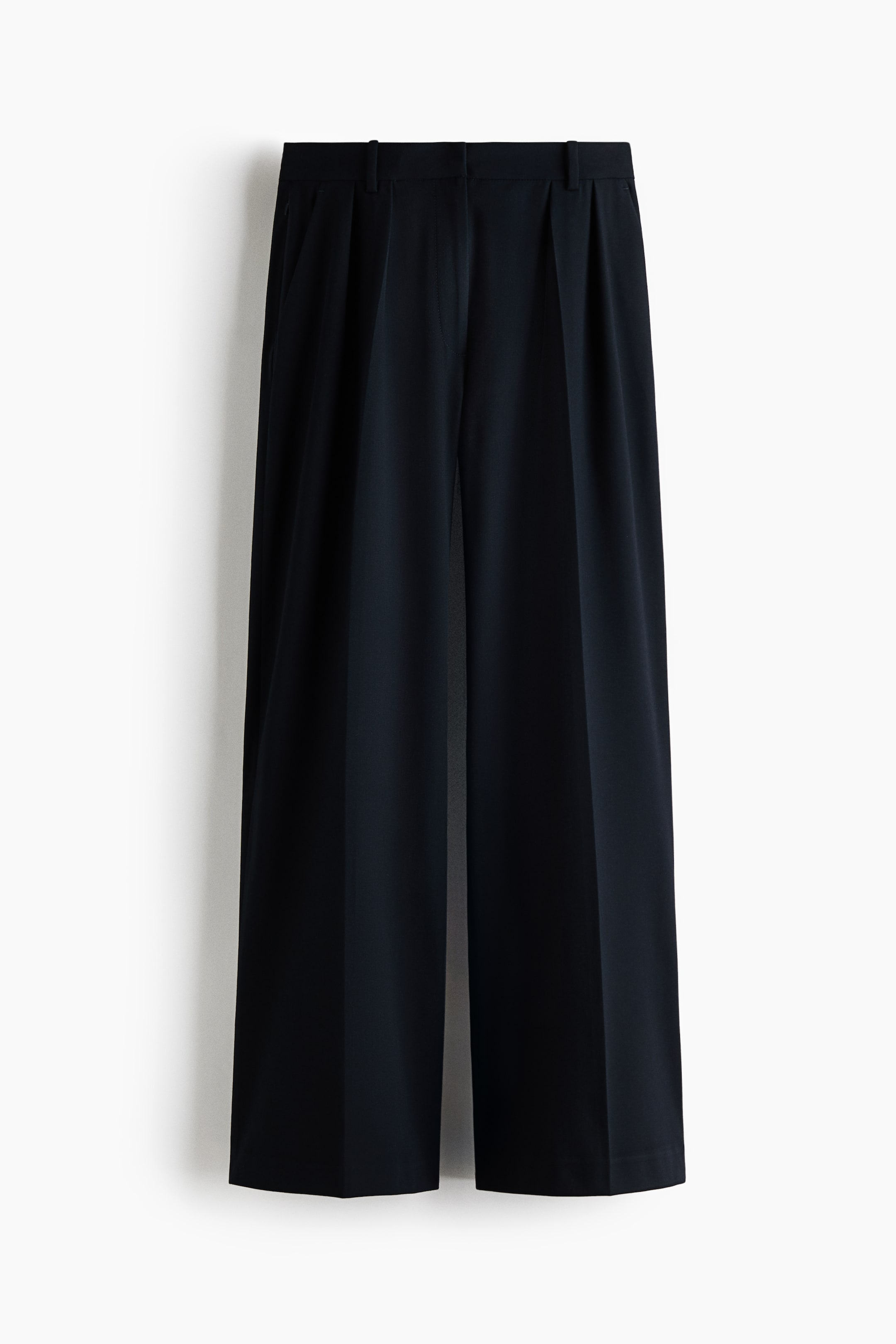 View larger image: These black wide-leg trousers are hanging front-facing, featuring a structured waistband with belt loops and double pleats. The trousers are draped in a relaxed fit, with sharp creases running down the center of each leg.