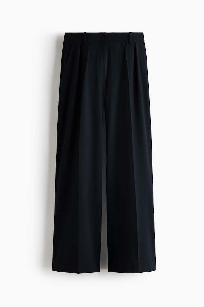 These black wide-leg trousers are hanging front-facing, featuring a structured waistband with belt loops and double pleats. The trousers are draped in a relaxed fit with sharp creases running down the centre of each leg. - 1