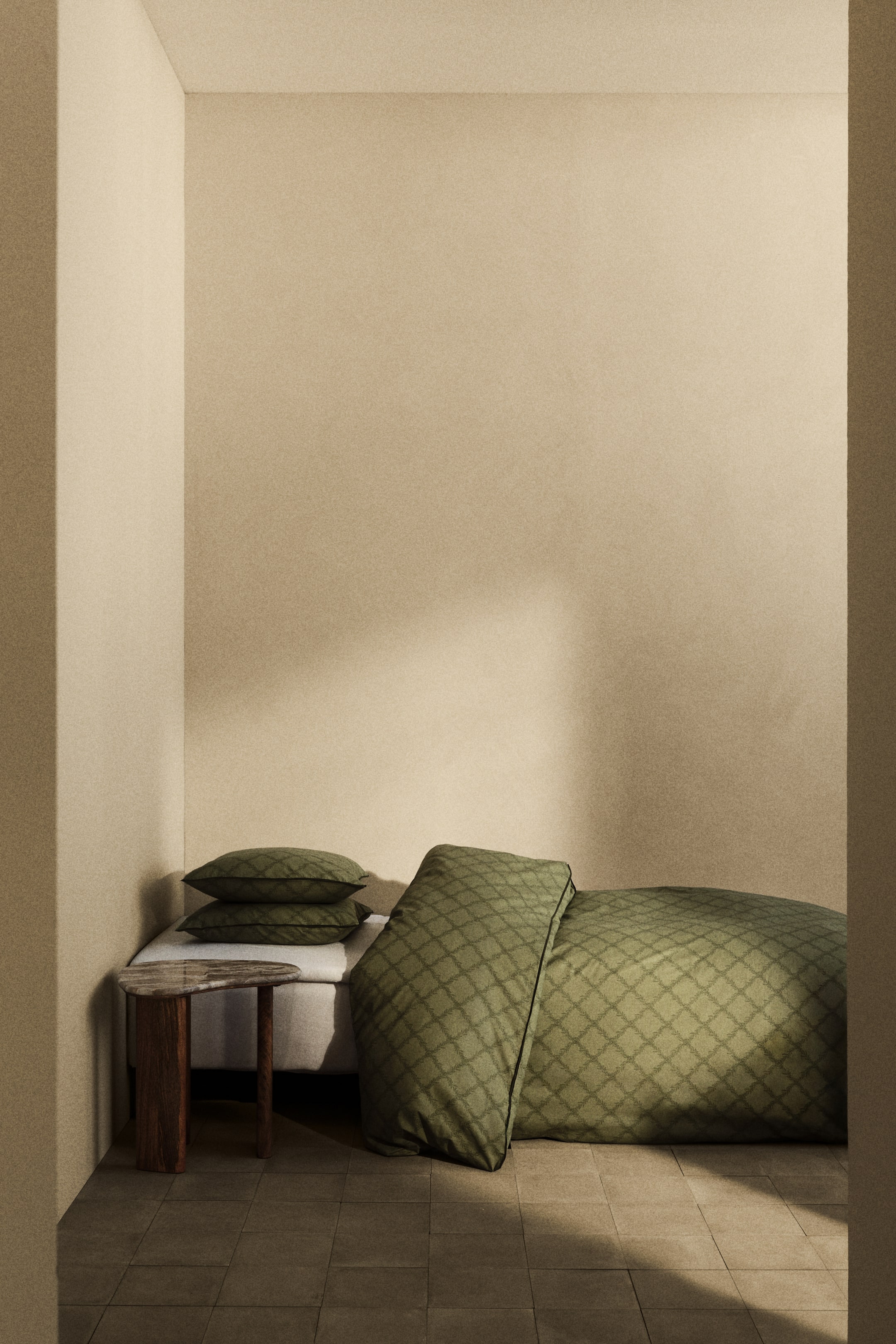 Nagyobb kép megtekintése: Egy olívazöld ágyneműhuzat garnitúra, amely teljes felületén geometrikus mintázatot és sötét szegélyt mutat a szélein. Az ágyneműhuzat részben összehajtva hever a padlón, bemutatva az elülső mintázatát, és két hozzáillő párnahuzat van egymásra helyezve az ágyon.
