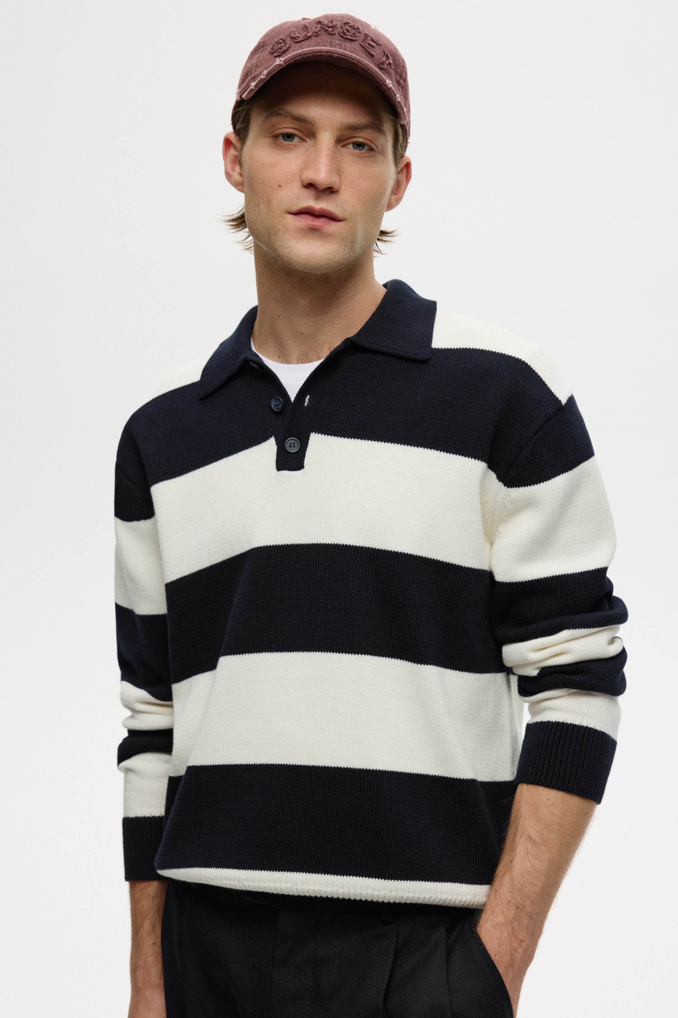 View larger image: A knitted polo shirt displays wide navy-blue and off-white horizontal stripes. It features a navy-blue polo collar with a two-button placket, ribbed cuffs, and a ribbed hem, with a white undershirt visible underneath.