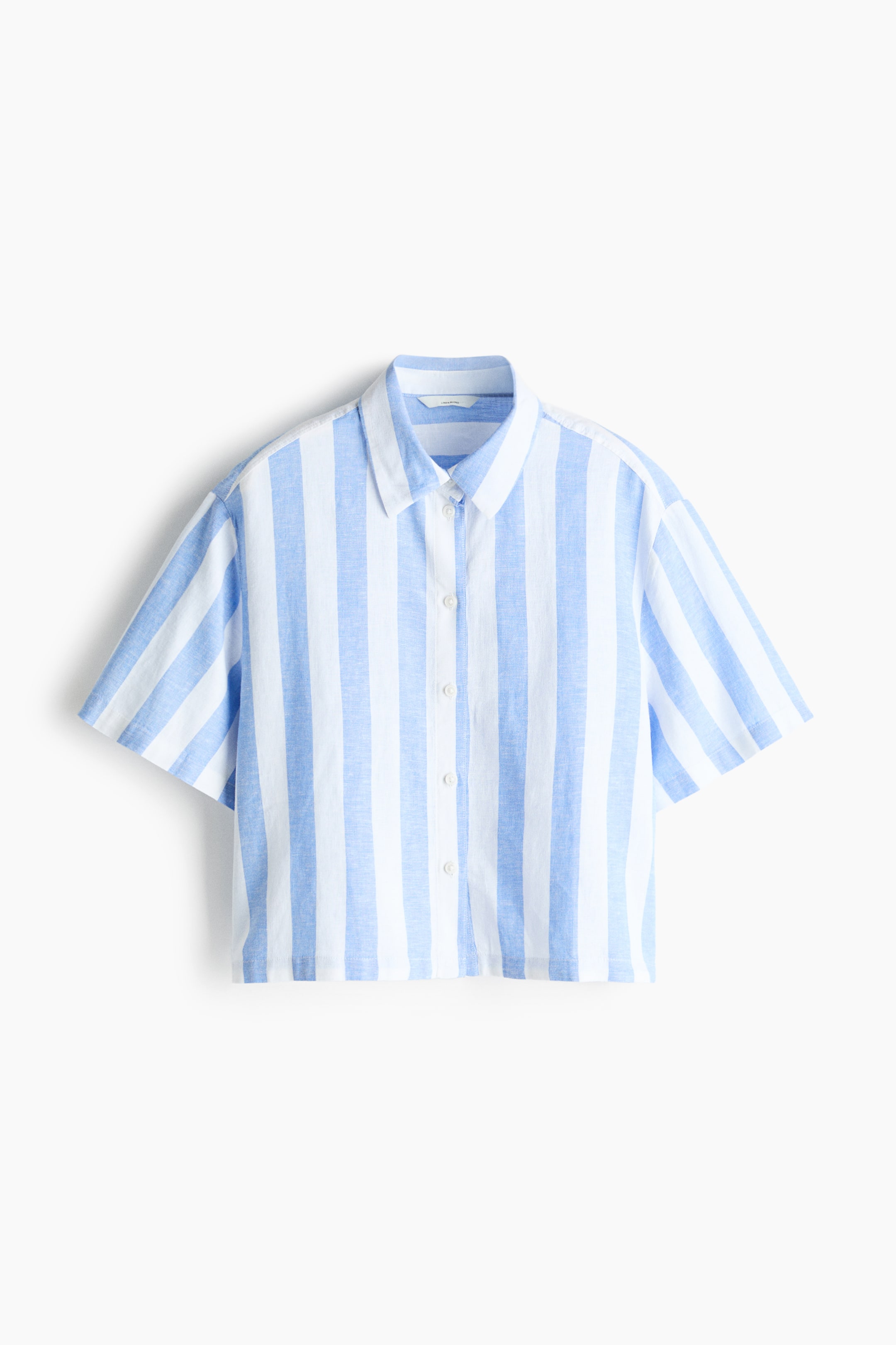View larger image: A blue and white vertically striped shirt is displayed front-facing, featuring short sleeves, a pointed collar, and a full button-front fastening with white buttons. The shirt is tailored to a cropped length.