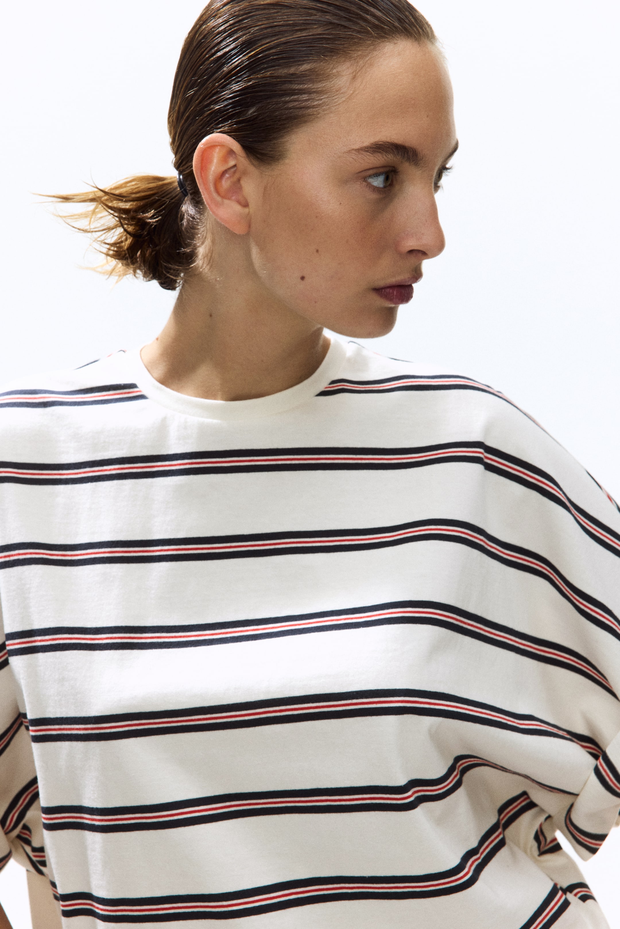 View larger image: "This cream-coloured striped top showcases horizontal stripes, each with a dark line and a thinner red line above. It features a round neckline and is styled with a relaxed fit, with its short sleeves rolled up."