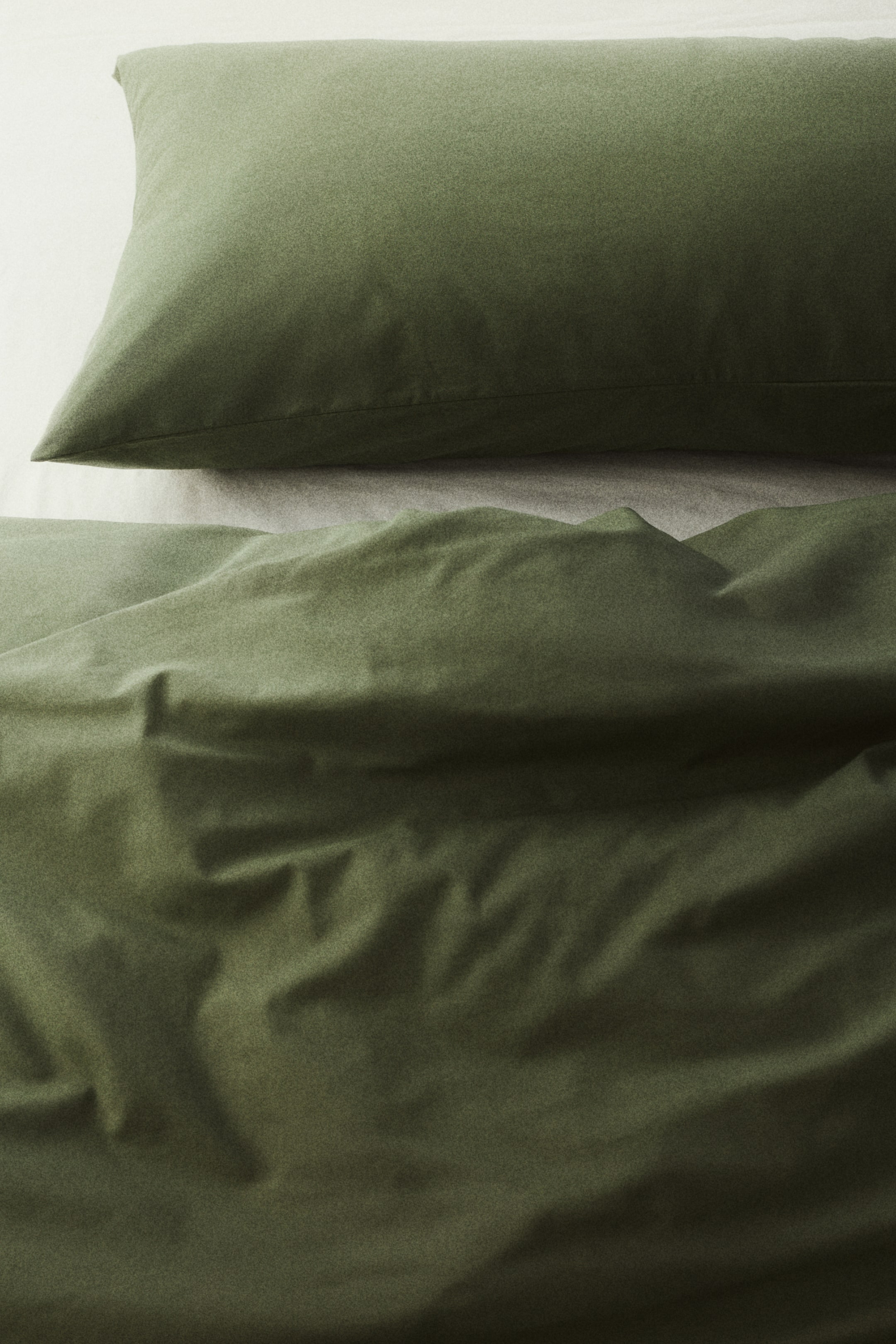 View larger image: A green pillowcase, fashioned from a fine-threaded cotton weave with a 144 thread count and an envelope opening, is displayed from the front. It rests upon a matching green sheet.