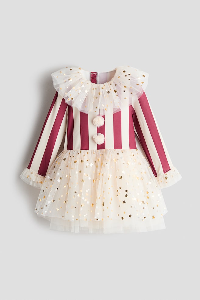 A childrenâs dress, shown from the front, featuring a burgundy and cream vertically striped bodice with long sleeves and ruffled tulle cuffs. The dress showcases a layered, ruffled tulle collar and a matching tulle skirt, both adorned with gold foil star prints, along with two fluffy cream pompoms on the chest. - 1