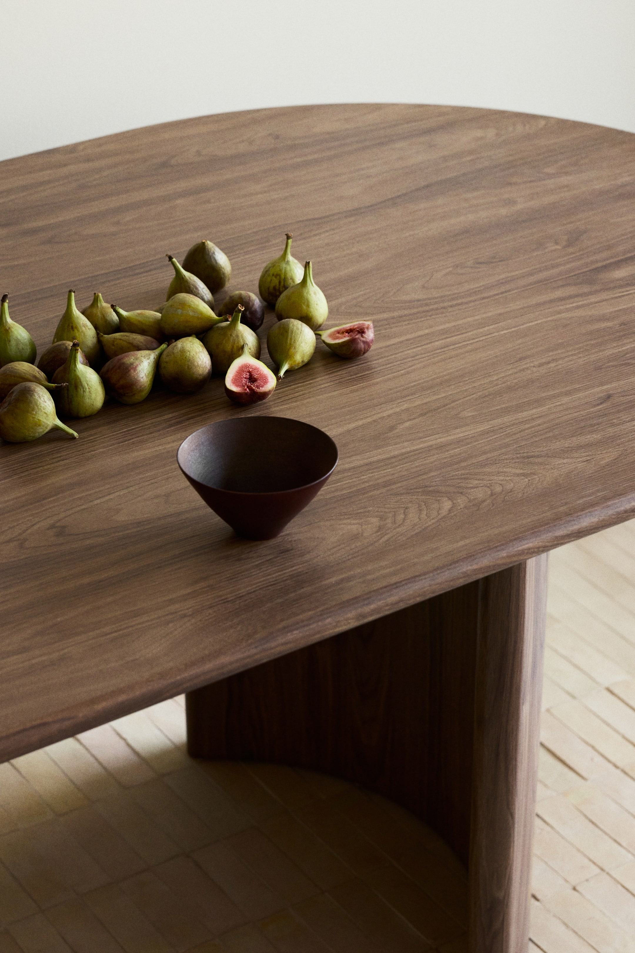 Agrandir l'image: La table en noyer présente un plateau sombre et finement veiné avec des bords lisses et arrondis, soutenue par un épais socle en bois courbé.