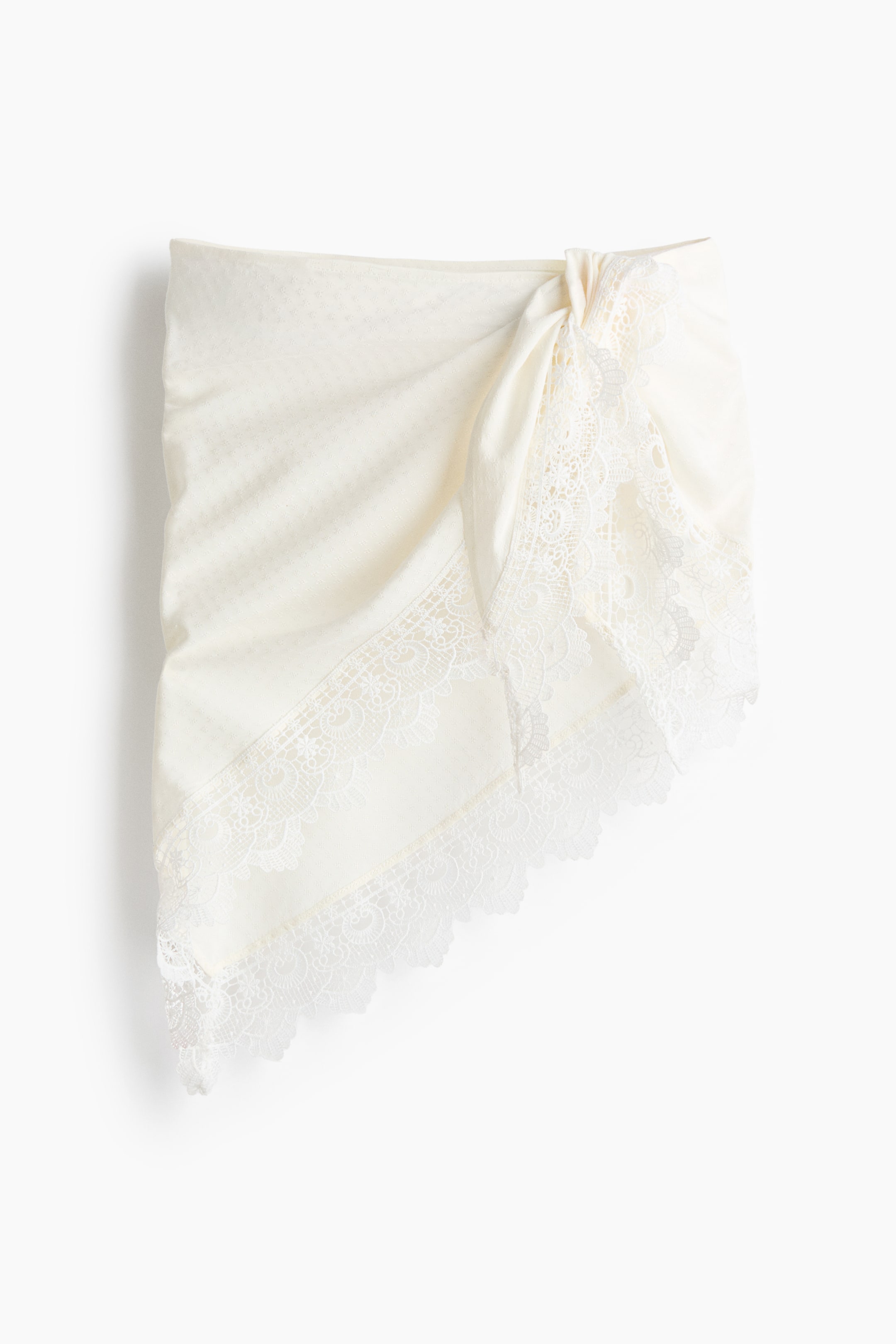 View larger image: The short triangle hip scarf is showcased from the front, boasting a cream textured viscose weave. It is tied on the right side, with delicate lace trims adorning its bottom edge.