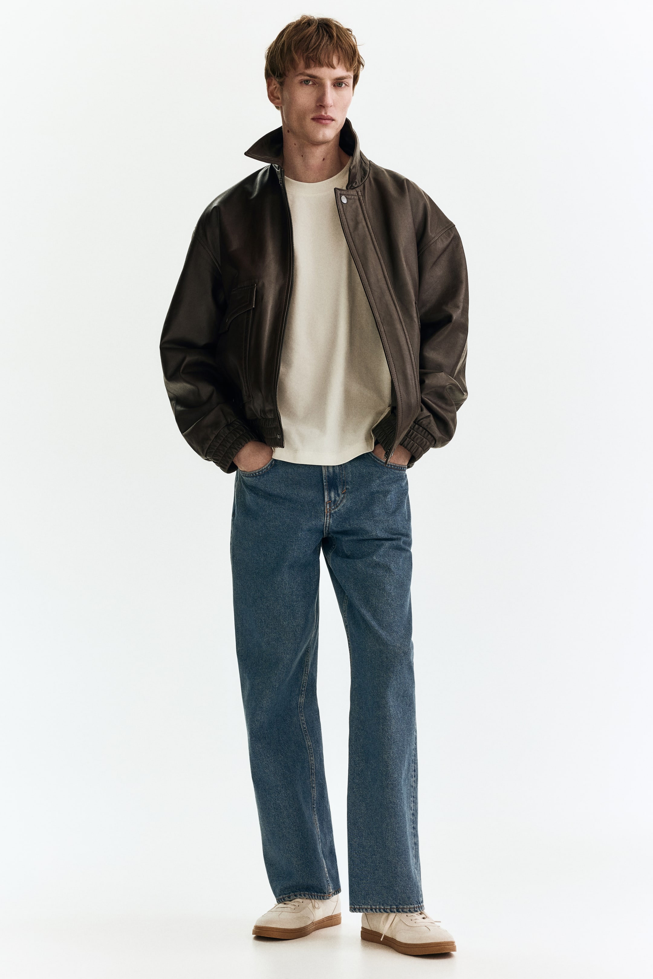 Größeres Bild anzeigen: Ein cremefarbenes, langärmeliges T-Shirt mit einem runden, gerippten Ausschnitt wird vom Model getragen, unter einer dunkelbraunen Jacke geschichtet.