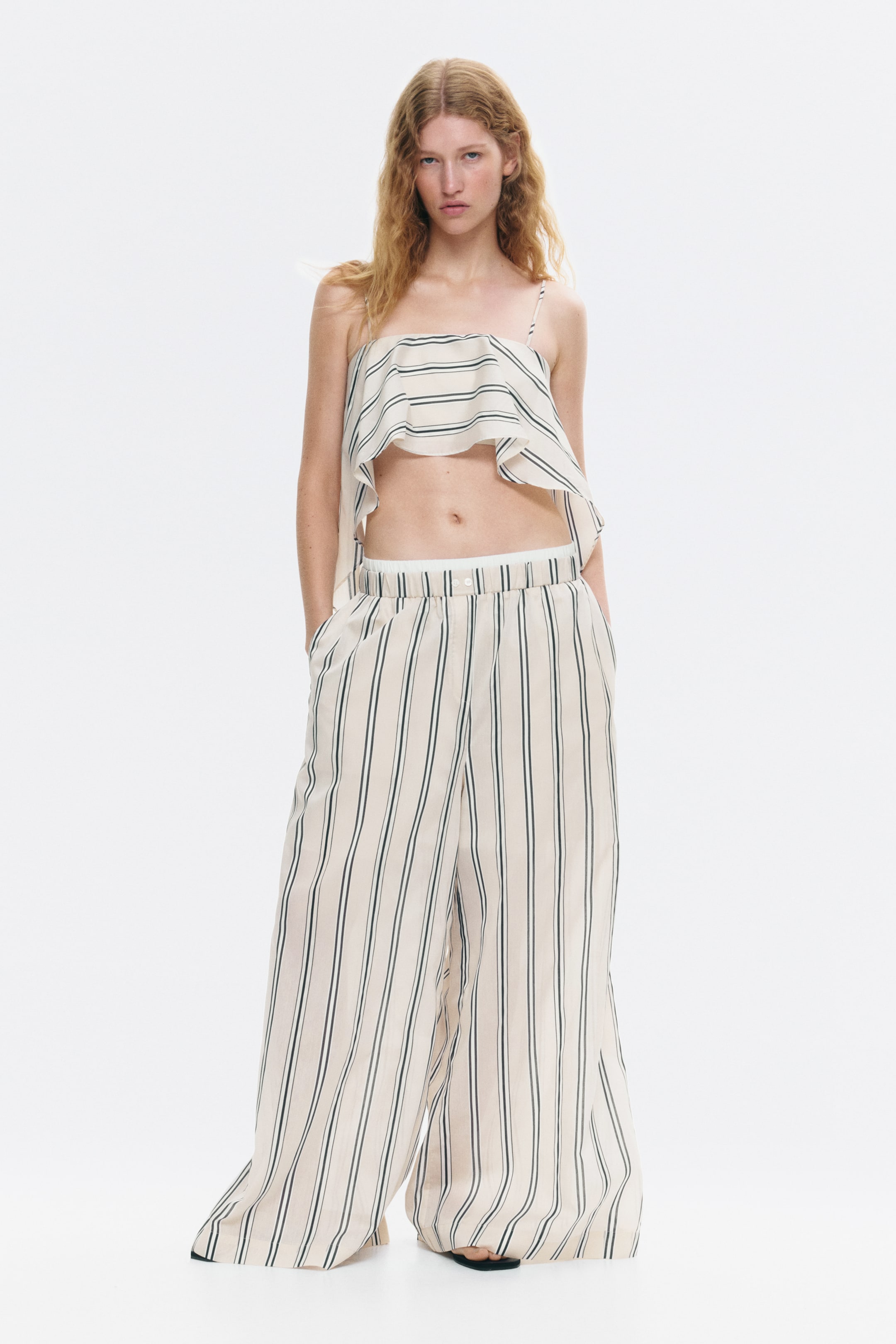 View larger image: A coordinating two-piece set, comprising a ruffled crop top and wide-leg trousers, is being showcased. The crop top boasts thin spaghetti straps and horizontal dark stripes on a light background, while the trousers display vertical dark stripes on a matching light background, featuring a high waist, side pockets, and an elasticated inner waistband.