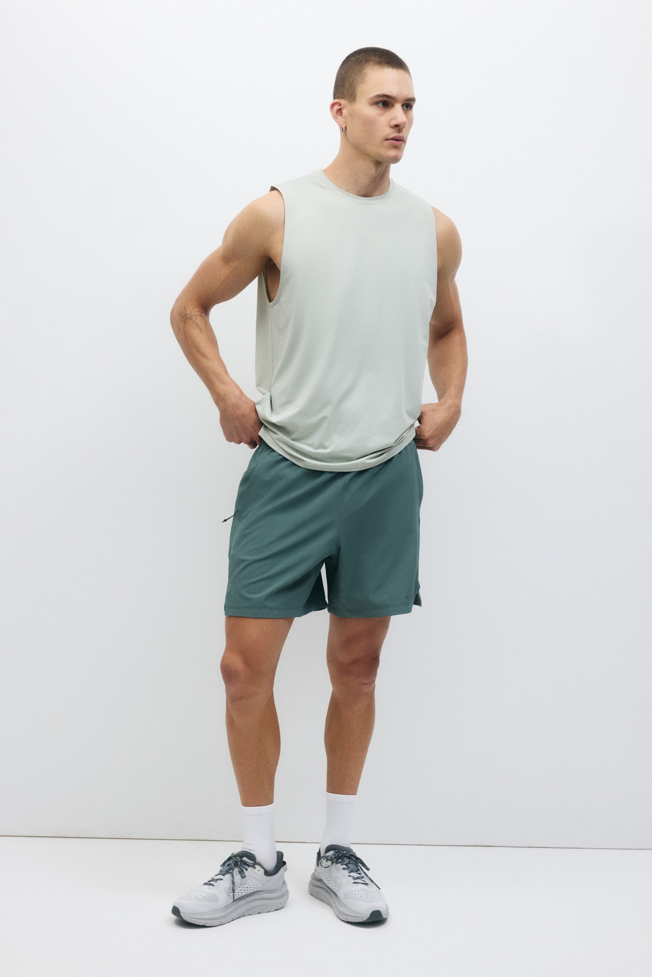 View larger image: A light green crew neck sleeveless top with a relaxed fit is paired with dark teal athletic shorts, featuring a subtle side zipper detail and an above-the-knee length.