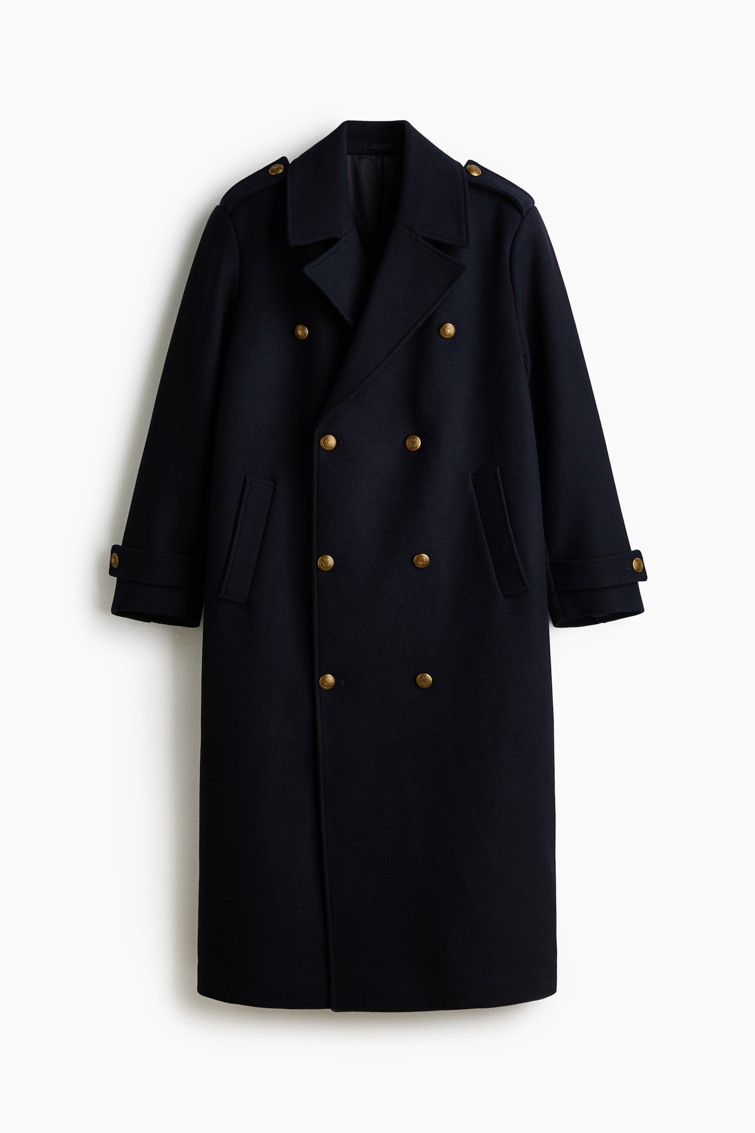 A navy blue double-breasted coat is hanging front-facing, showcasing wide notch lapels, shoulder epaulettes, and angled welt pockets. The coat features a double-breasted closure with gold-toned buttons and adjustable buttoned straps at the cuffs.