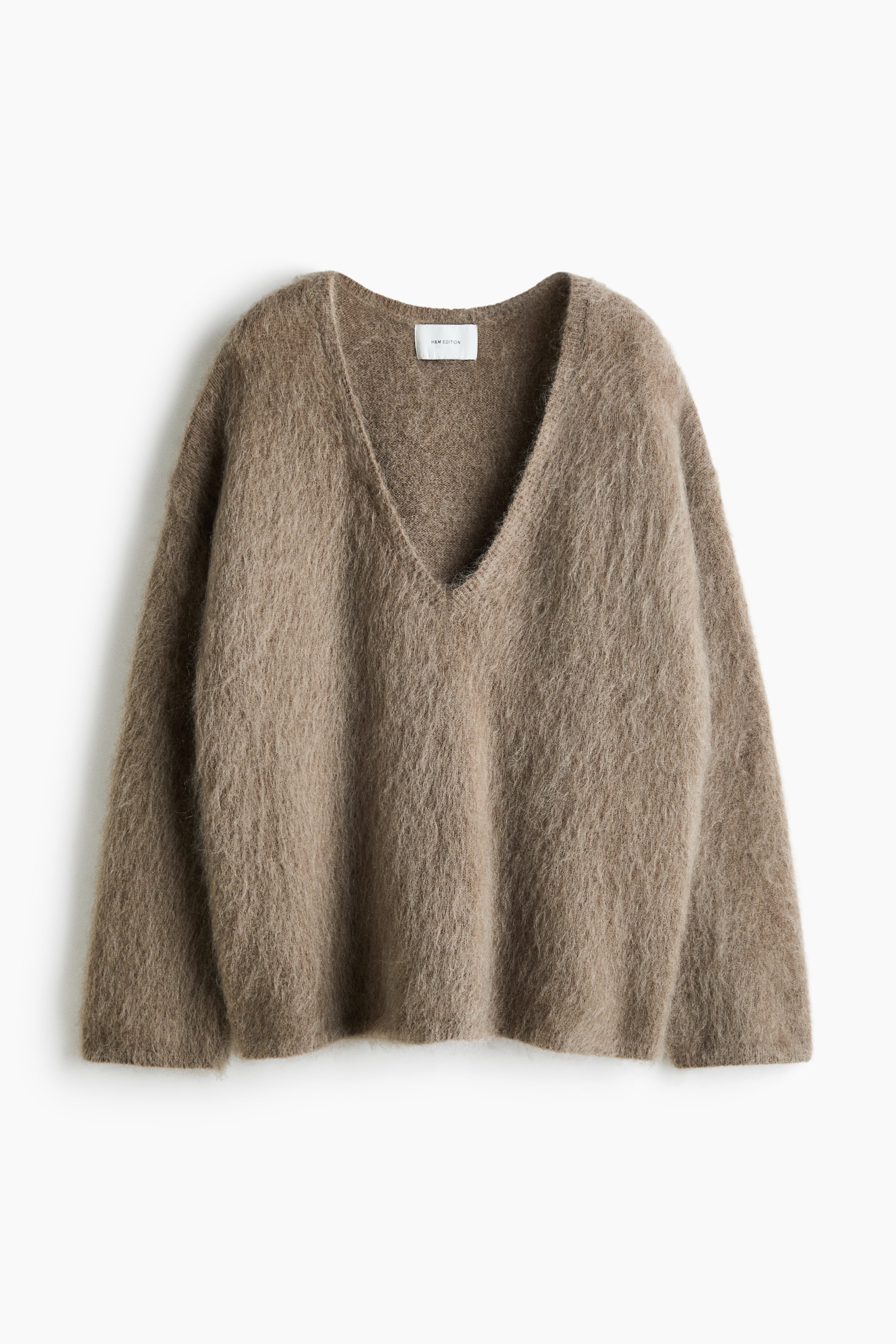 View larger image: An oversized, taupe-brown sweater with a fuzzy, brushed knit texture is shown from the front. The sweater features a deep rib-trimmed V-neckline, dropped shoulders, and long sleeves with subtle ribbing at the cuffs and hem.