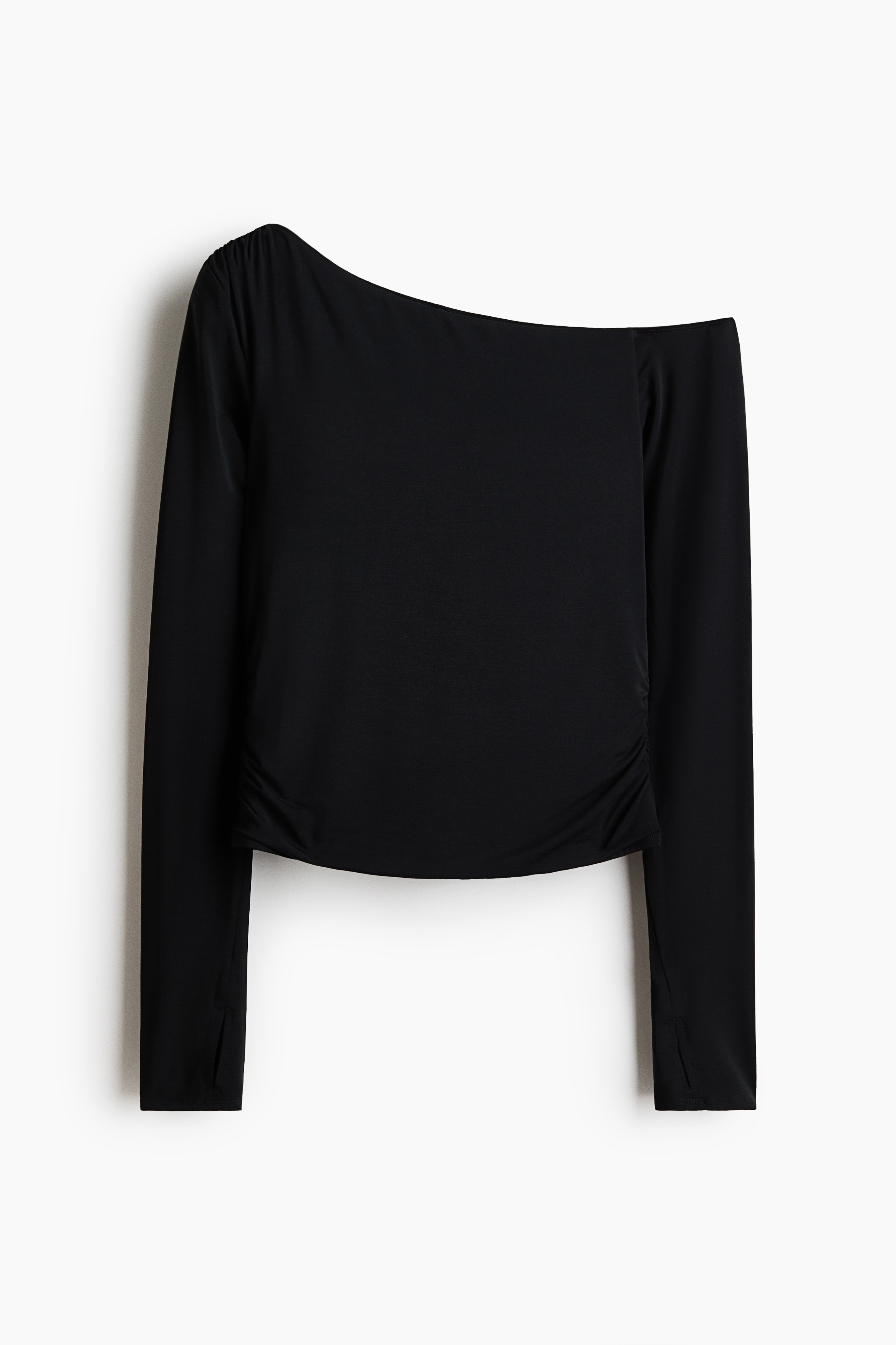 Un top sport negru cu mânecă lungă și SoftMove este purtat de model, evidențiind un design asimetric, cu umerii goi, și orificii pentru degete. Se vede dedesubt un sutien sport alb, iar ținuta este completată de pantaloni scurți sport negri.
