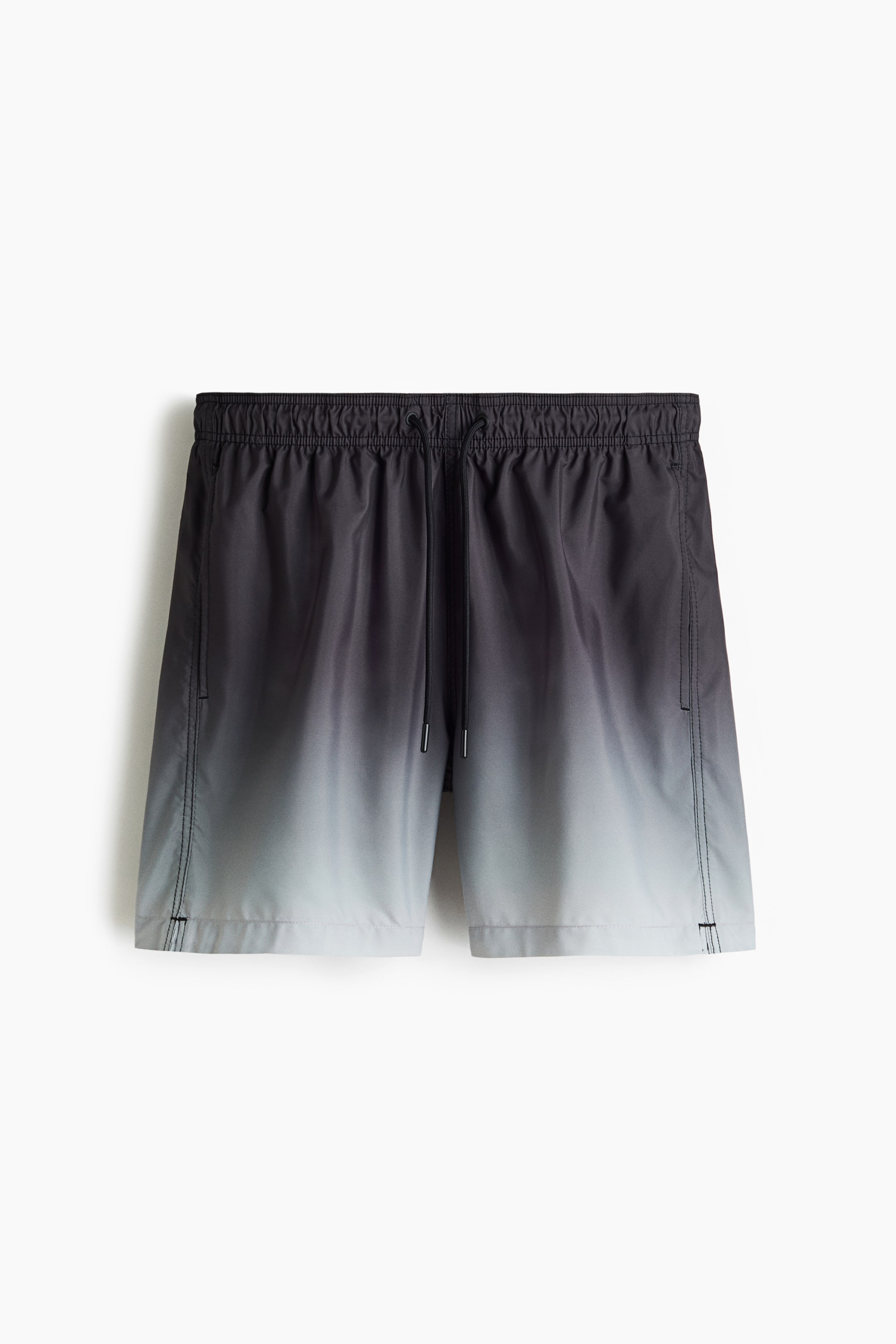 View larger image: Swim shorts are showcased from the front, exhibiting a black to light grey ombre pattern that transitions from dark at the top to light at the bottom. They come with a covered elastic waistband, a drawstring, and side pockets, with a small slit on one side of the hem.