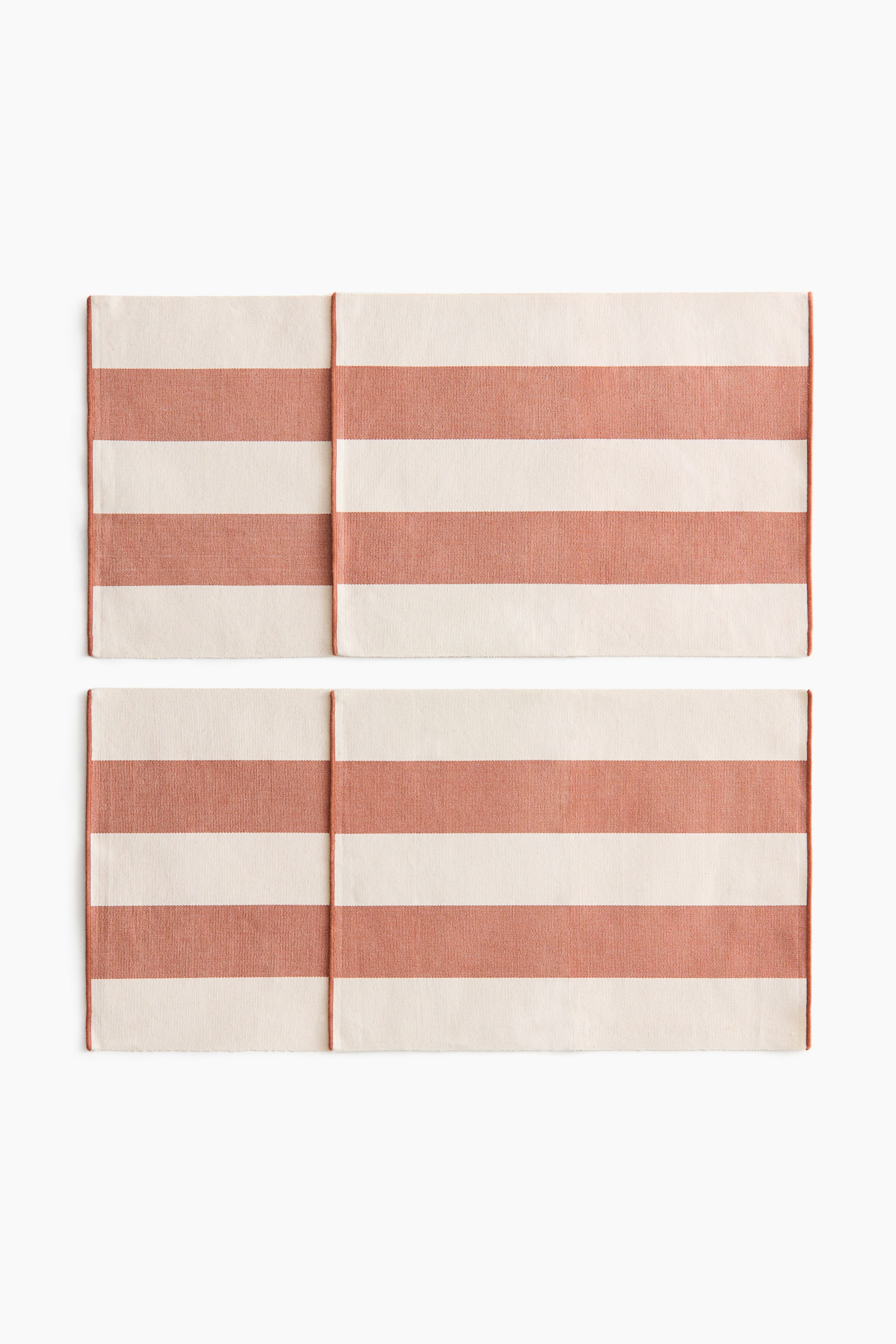 View larger image: Two rectangular placemats are presenting front, each featuring wide horizontal stripes. They are showing alternating bands of off-white and reddish-brown.