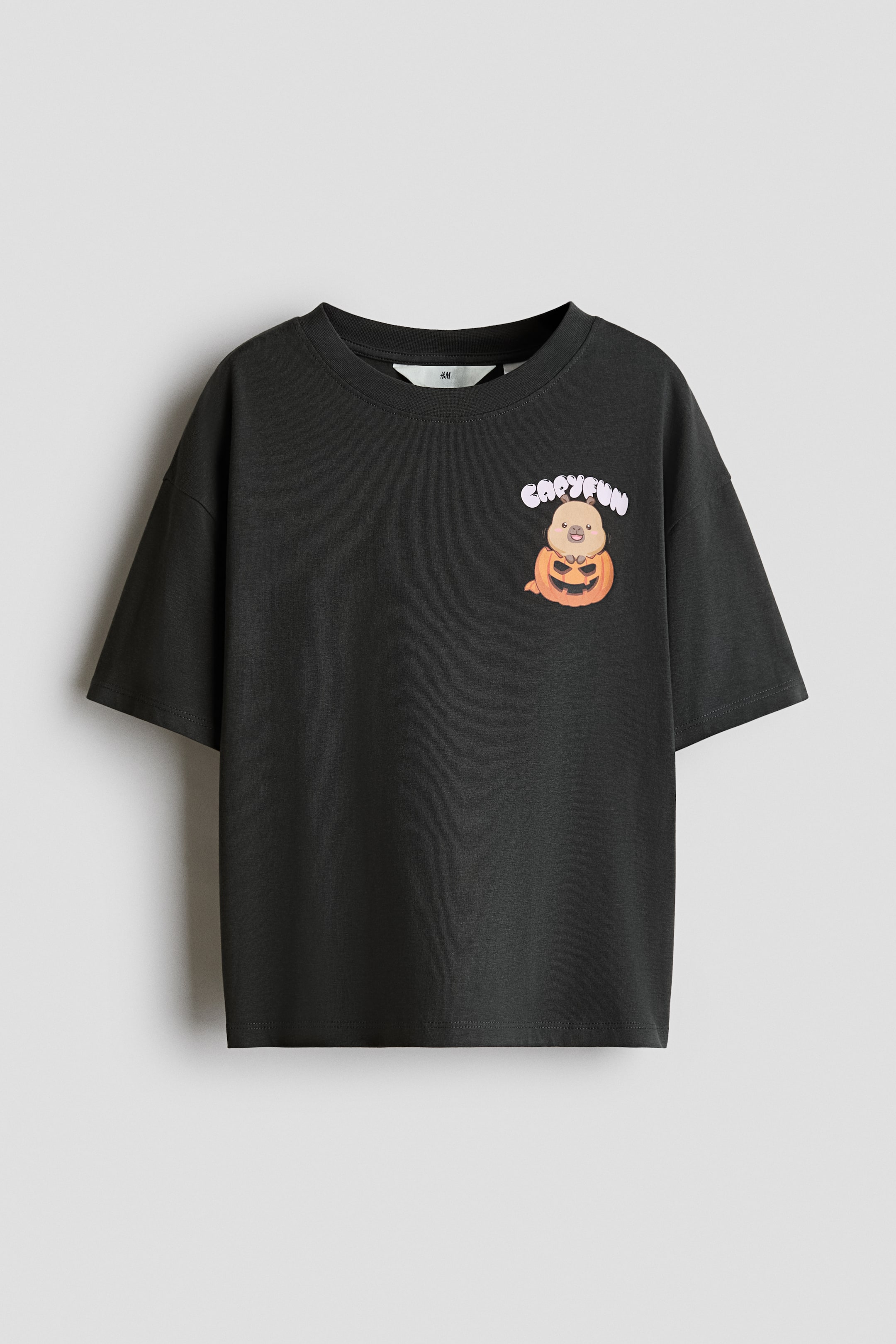 View larger image: A dark grey cotton jersey T-shirt is shown from the front, featuring a round neckline, dropped shoulders, and short sleeves. The T-shirt displays a small graphic print on the left chest depicting a cartoon capybara inside a jack-o'-lantern under the text "CAPYFUN".
