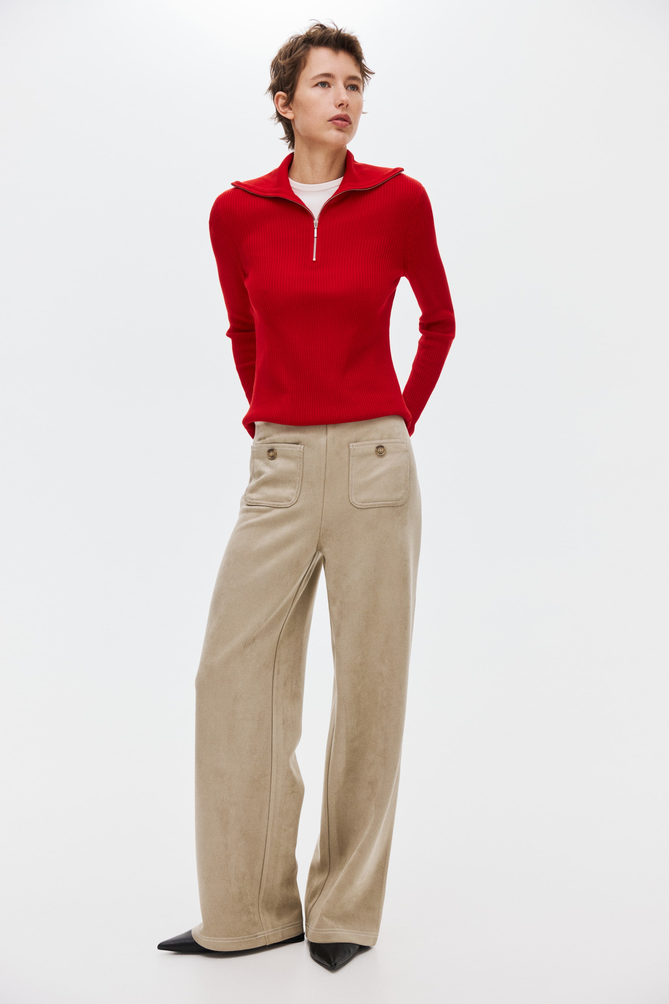 View larger image: A red ribbed-knit quarter-zip sweater features a spread collar and long sleeves, layered over a white T-shirt. It is styled with beige wide-leg trousers featuring two front patch pockets with button detailing and vertical seams, and covering black pointed-toe shoes.