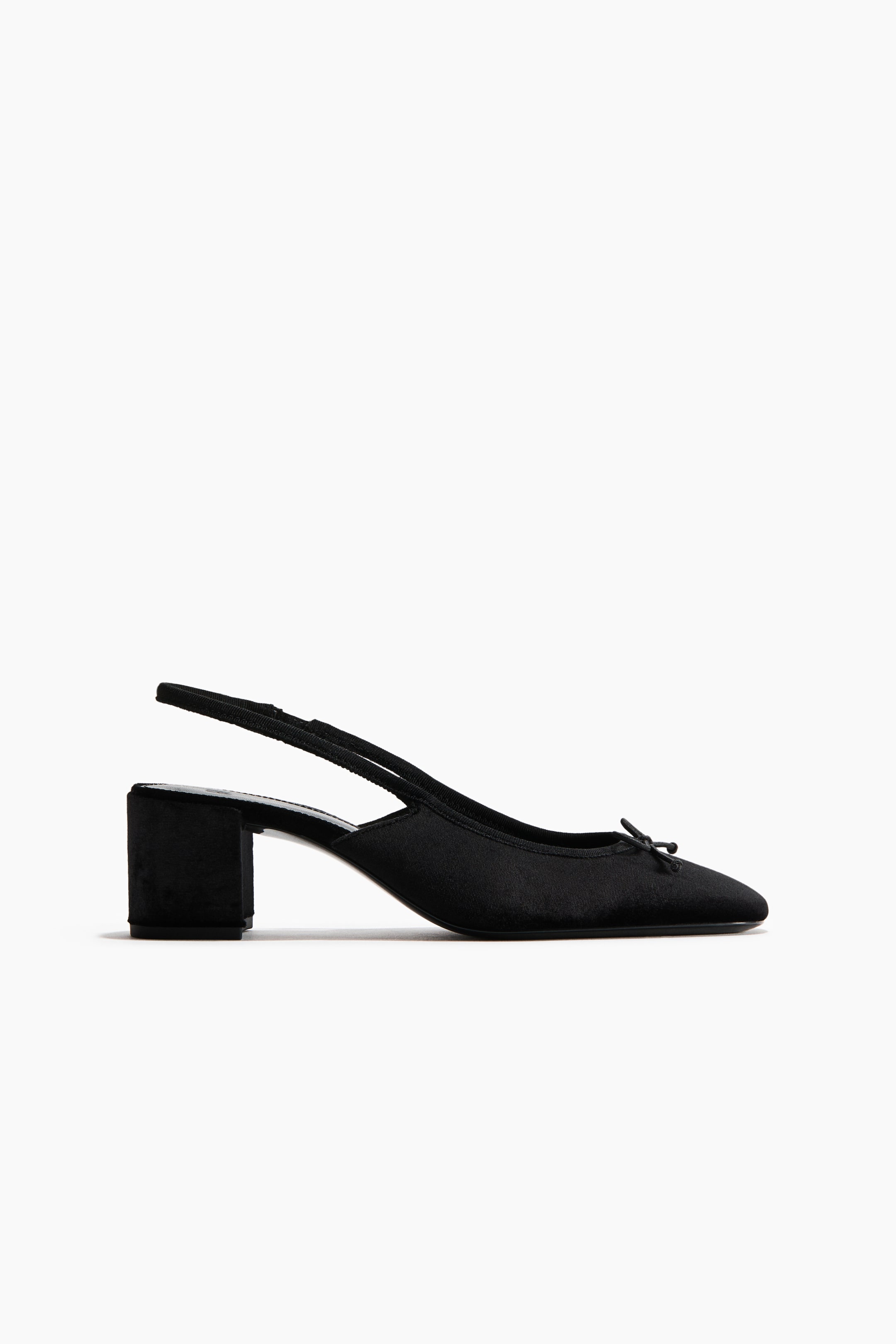 View larger image: A black slingback shoe is shown in side profile, featuring an almond-shaped toe with a small decorative bow at the front. The shoe rests on its low, covered block heel, with a narrow elasticated strap extending around the back.