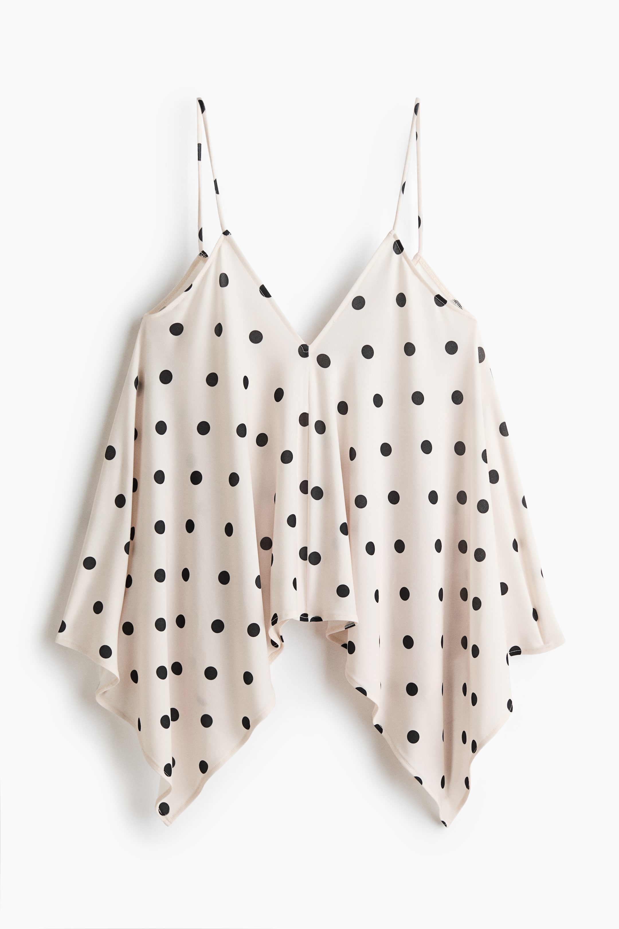 View larger image: This cream camisole top, adorned with black polka dots, highlights a V-neckline and delicate spaghetti straps. It features a flowy, asymmetrical hemline with pointed corners, perfect for a chic and modern look.