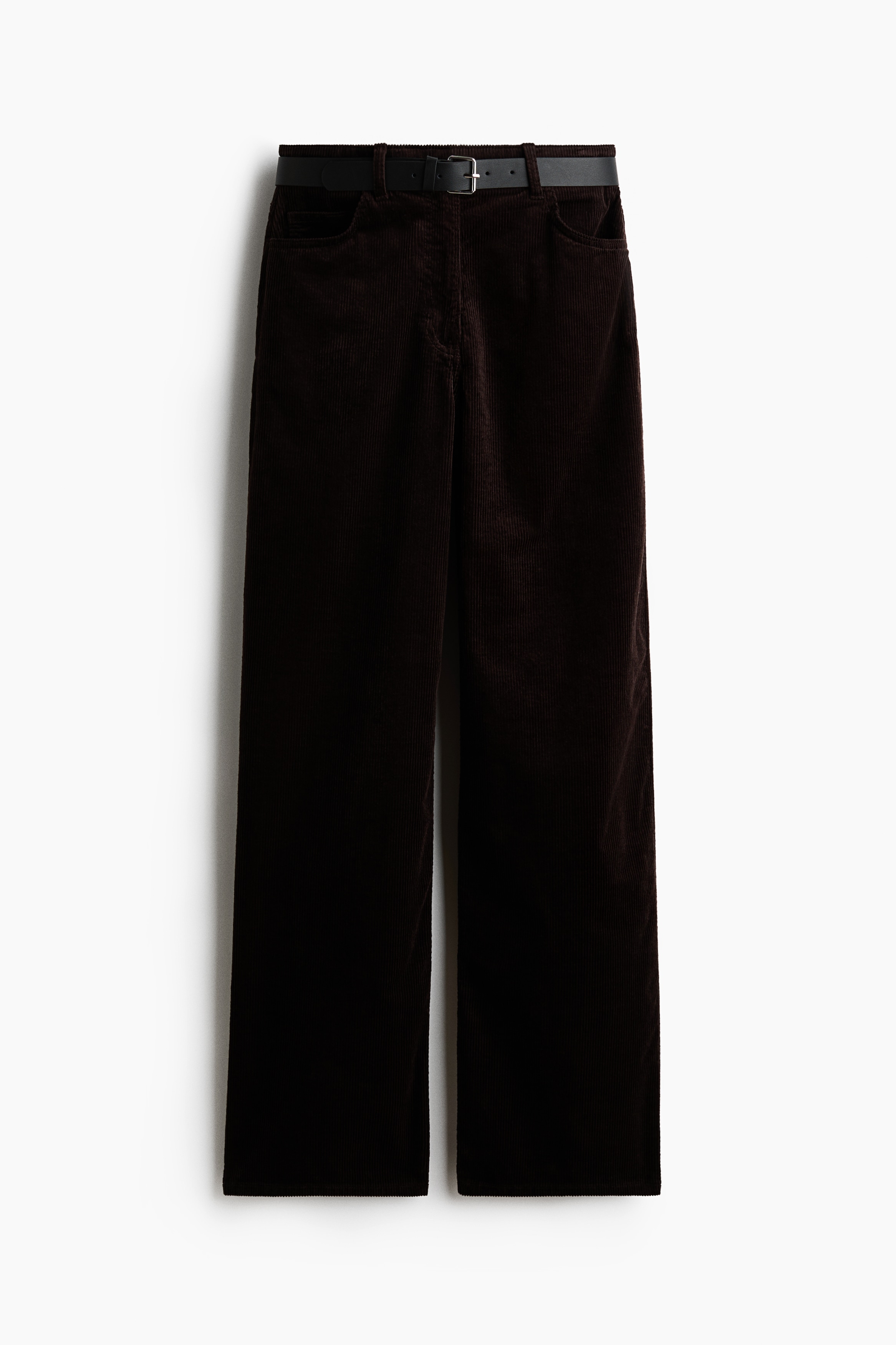 Dunkelbraune Cordhose mit geradem Bein und hohem Bund, getragen vom Model, das mit den Händen in den vorderen Taschen steht. Die Hose ist mit einem schwarzen Gürtel mit Schnalle gesichert und mit einem grauen T-Shirt kombiniert, das in den Bund gesteckt ist.