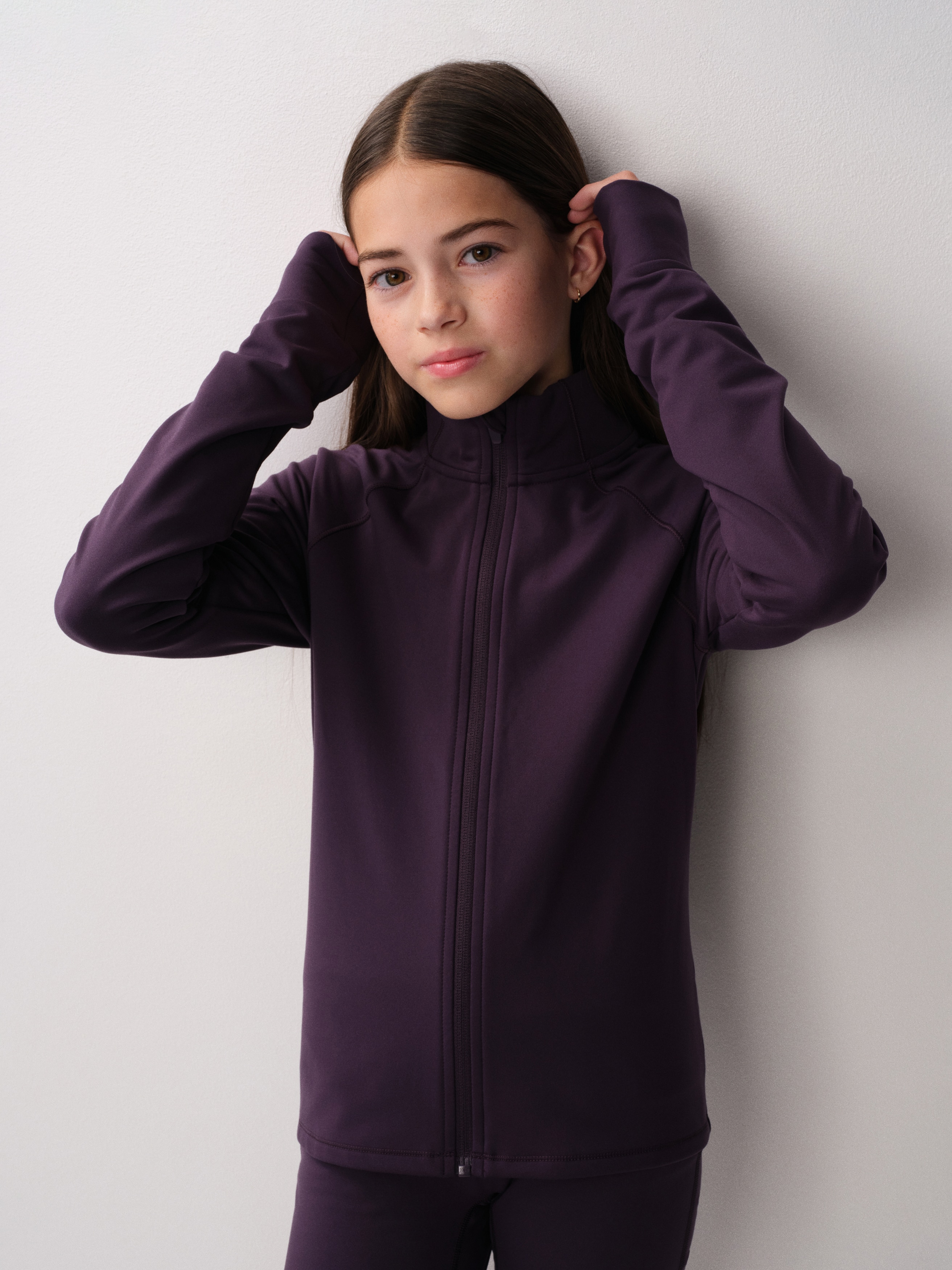 A dark purple zip-up jacket is shown facing front, featuring a high stand-up collar and long raglan sleeves with wide, structured cuffs. The jacket has a straight, slightly cropped hemline and a full-length matching zip down the centre.