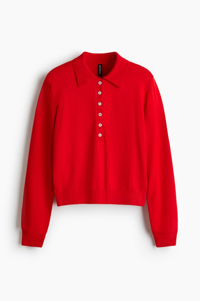 En rød poloshirt præsenterer sin frontudsigt. Den er lavet af en fin strik og har en krave og en knapstolpe med fem hvide knapper. Skjorten er designet med let sænkede skuldre og lange ærmer, og er afsluttet med ribkanter ved manchetterne og kanten. - 1