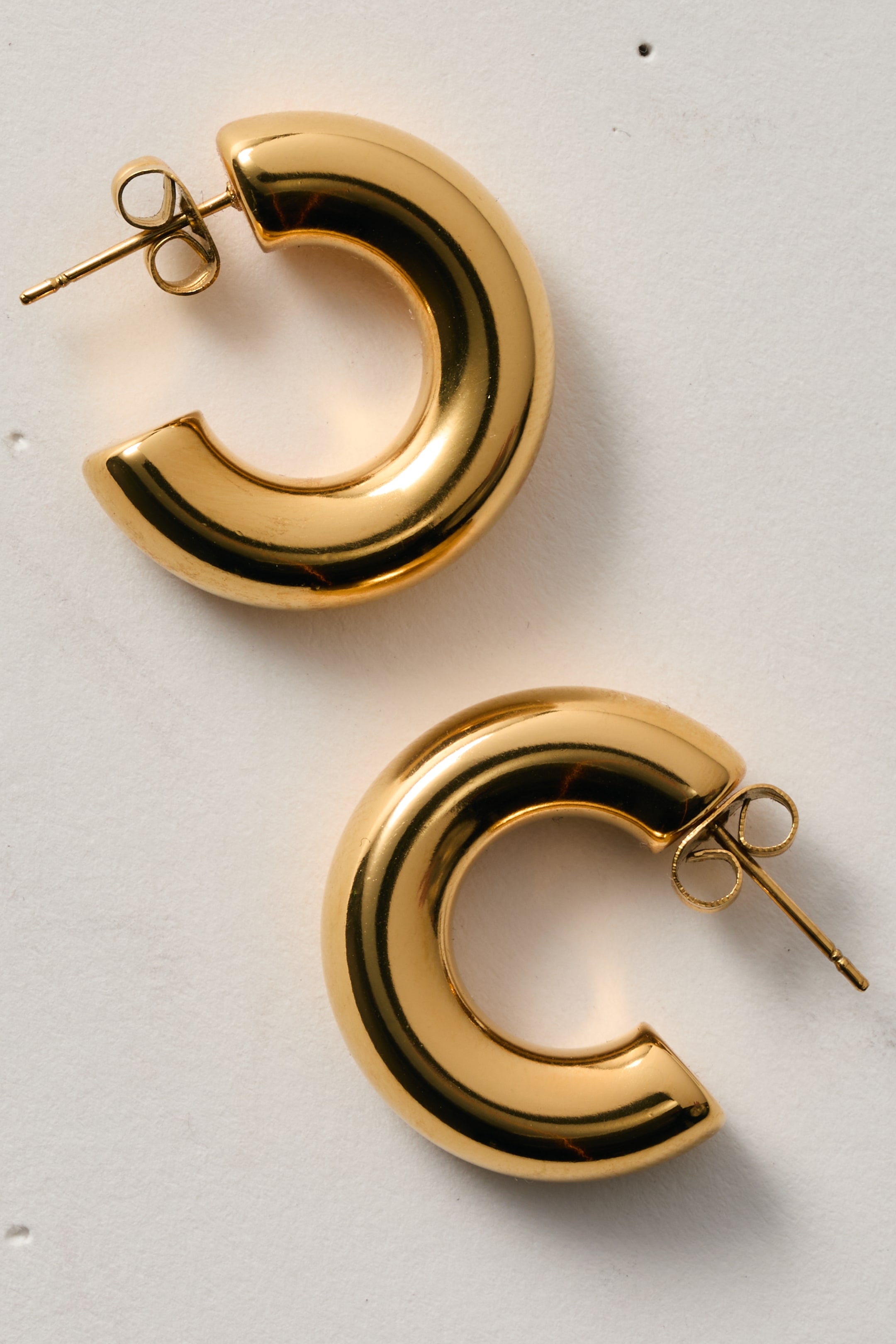View larger image: Hoop earrings are showcasing a lustrous, gold-toned metal with a bold, C-shaped design. Each earring features a visible post-back closure.