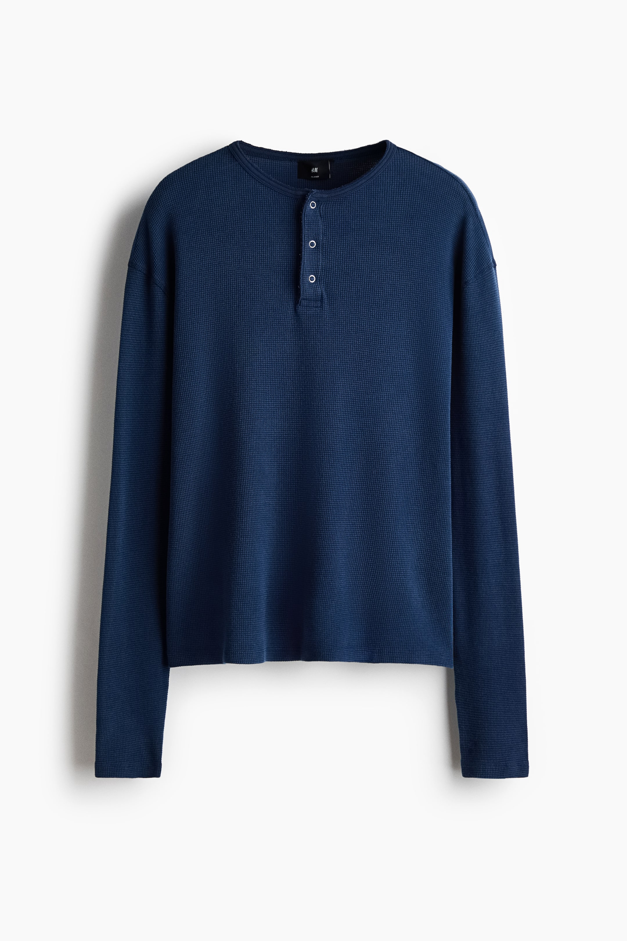 Grotere afbeelding bekijken: Een Henley-top met lange mouwen in donkerblauwe wafelstructuur katoenen jersey toont een ronde halslijn met een knoopsluiting met drie knopen. Het heeft een ontspannen pasvorm met lange mouwen en een recht gesneden zoom, getoond vanaf de voorkant.