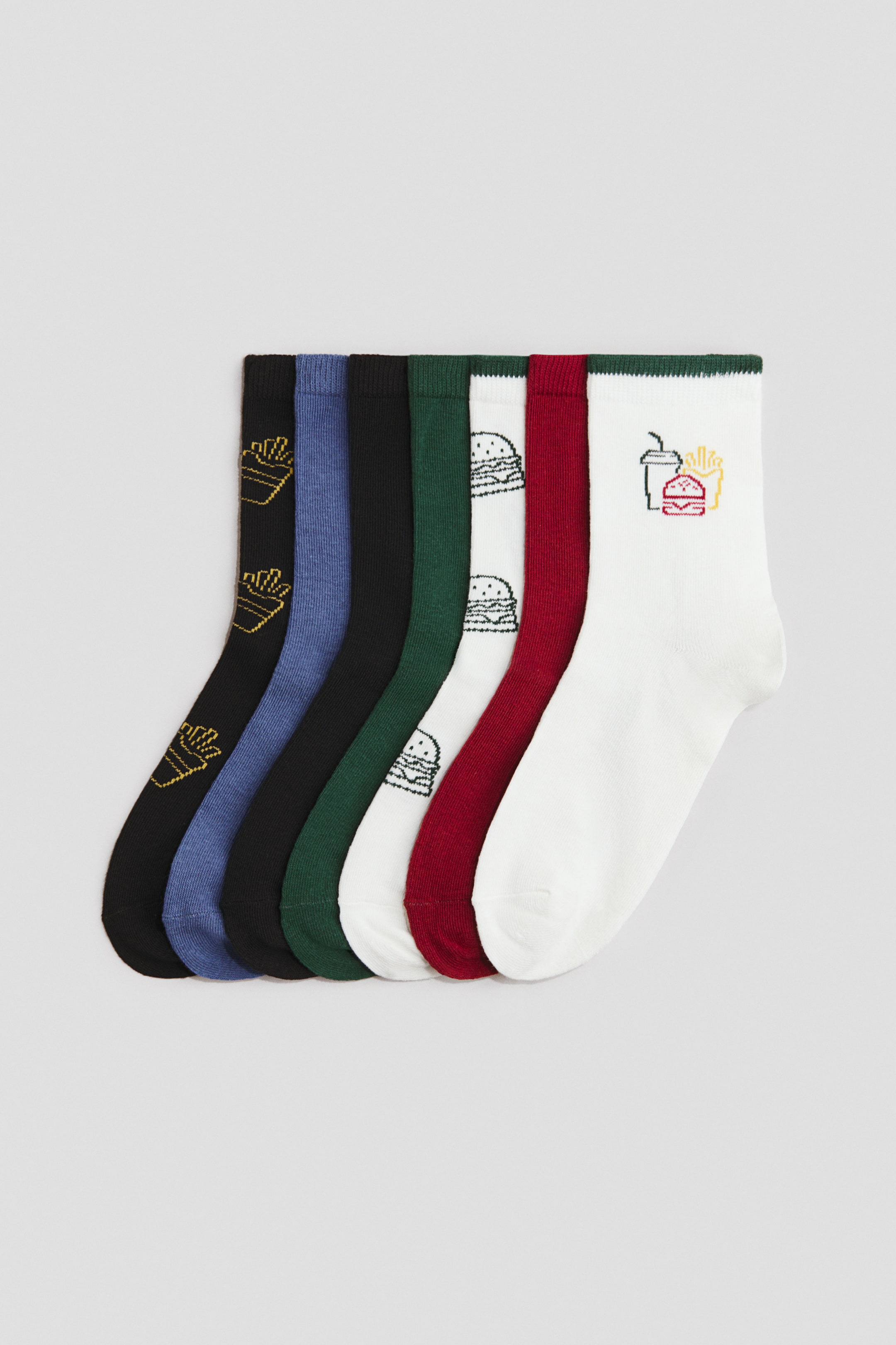View larger image: A set of seven socks is laid flat and fanned out, showcasing their side profiles. The socks exhibit a variety of colours, including black, blue, dark green, white, and dark red. Distinctive patterns include yellow outlined French fries on a black sock, black outlined hamburgers on a white sock, and a multi-coloured embroidered graphic of a hamburger, French fries, and a drink near the cuff of another white sock, which also features a dark green cuff trim.