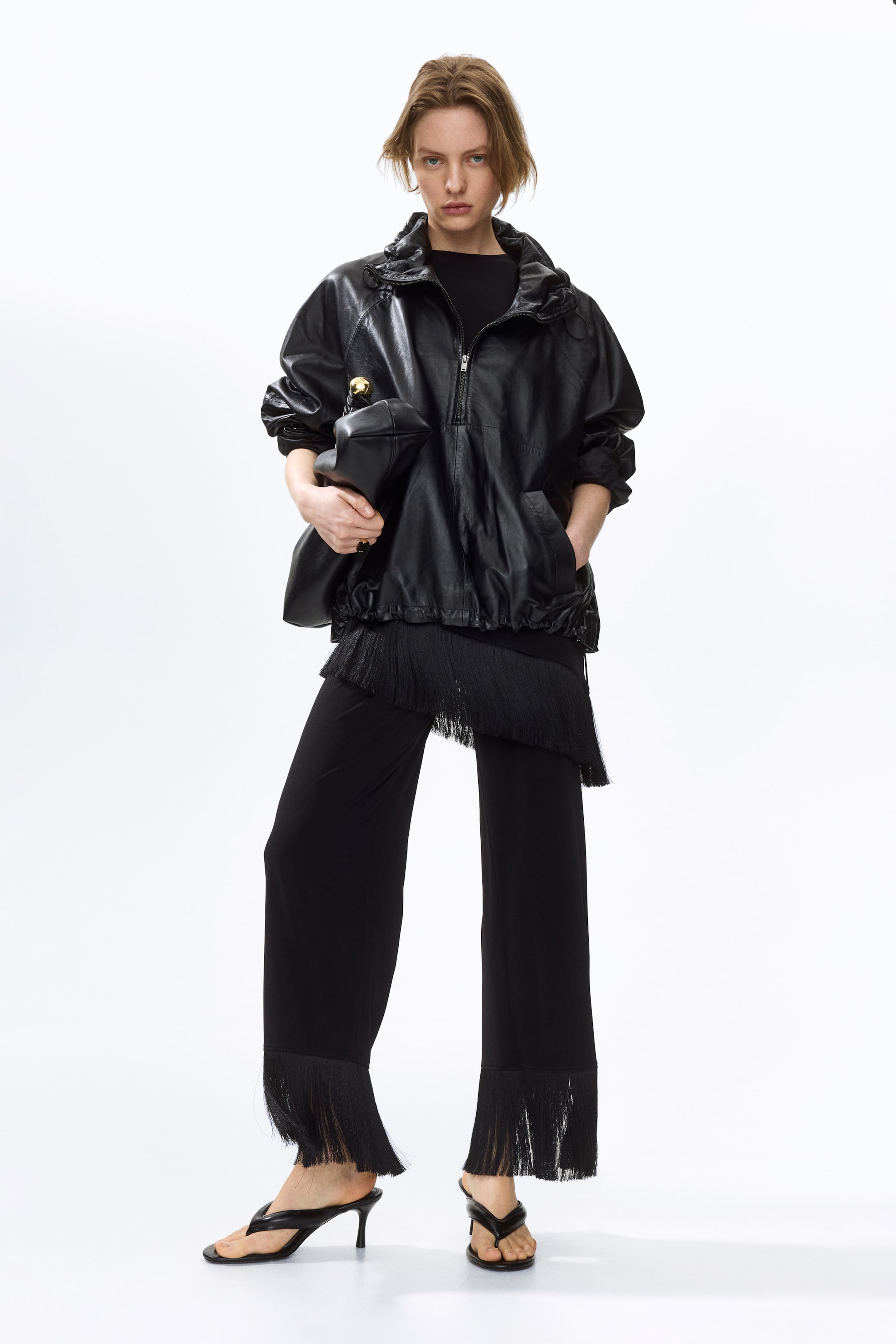 Ampliar la imagen: Pantalones de jersey negro suave con cintura elástica, piernas anchas y dobladillos con flecos son llevados por la modelo, quien está de pie mostrando su longitud completa.