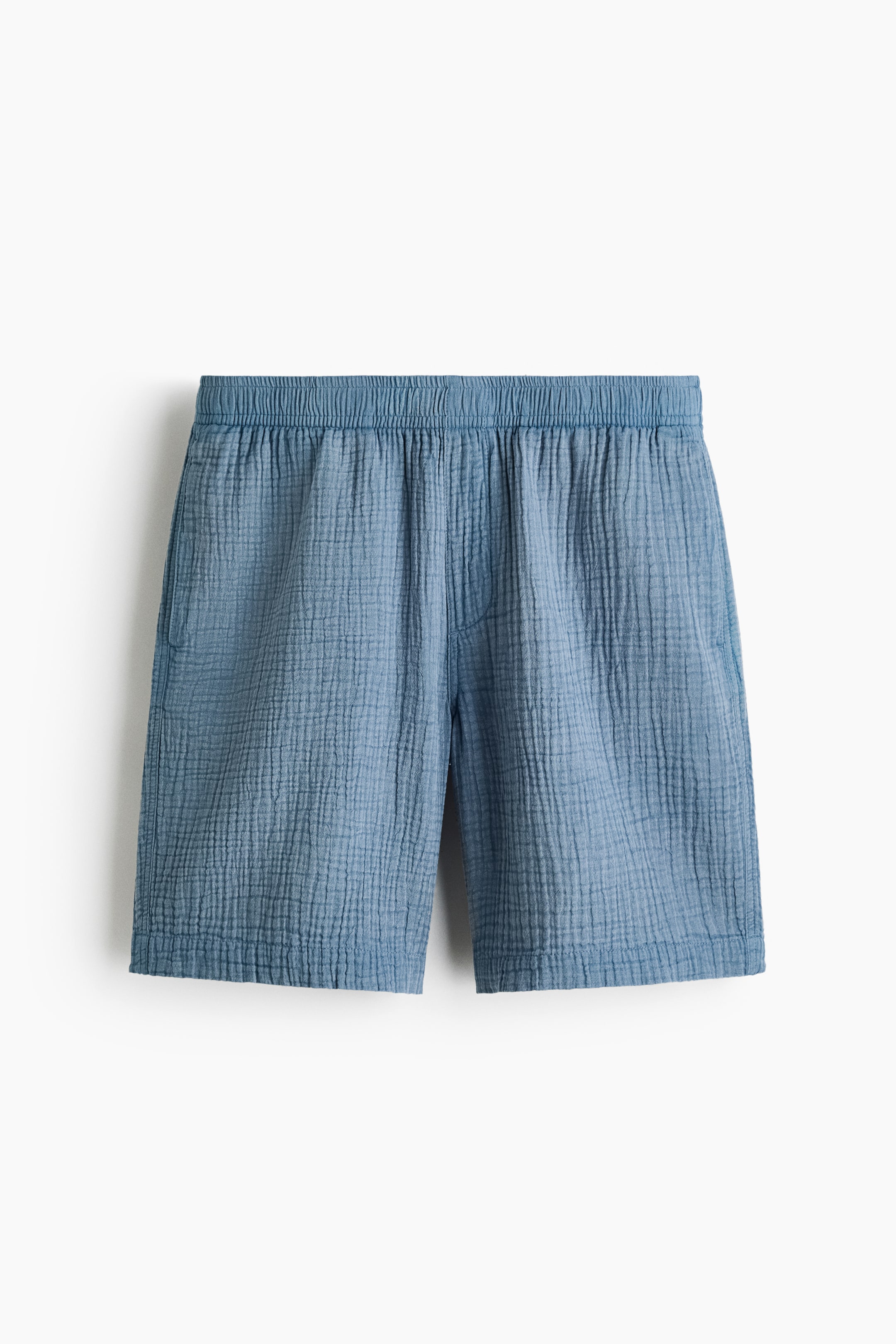 Se større billede: Blå shorts viser en krøllet, gaze-lignende tekstur og en elastisk talje. De har sidelommer med skrå åbning og en lige kant, præsenteret fra en frontvisning.