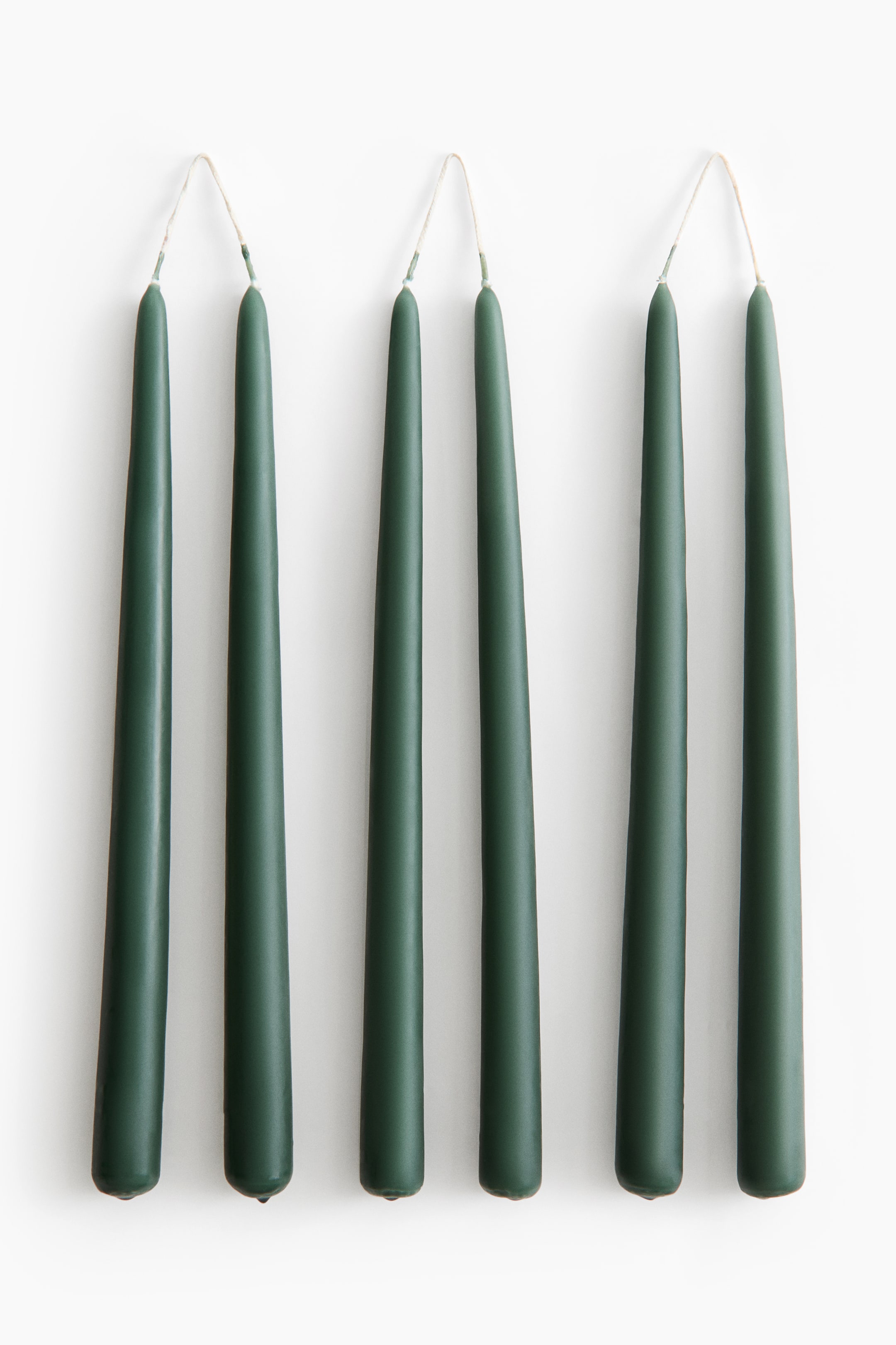 Agrandir l'image: Trois paires de bougies coniques vert foncé sont suspendues verticalement en rangée, chaque paire étant reliée en haut par une mèche blanche continue. Les bougies s’affinent progressivement d’une base plus large vers une pointe étroite, mettant en valeur une finition mate et lisse.