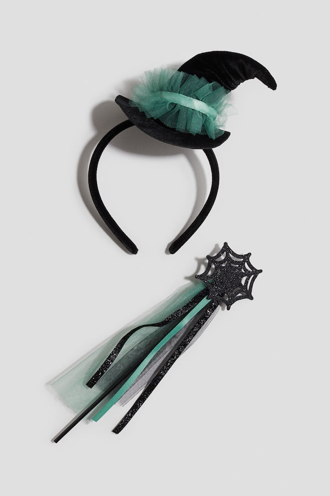 A fancy dress set is featuring a black Alice band with a small, pointed black hat attached, which is trimmed with ruffled green tulle and a green ribbon band. A matching wand is also included, having a black glittery spiderweb top and flowing green and black tulle and glitter ribbons. - 1