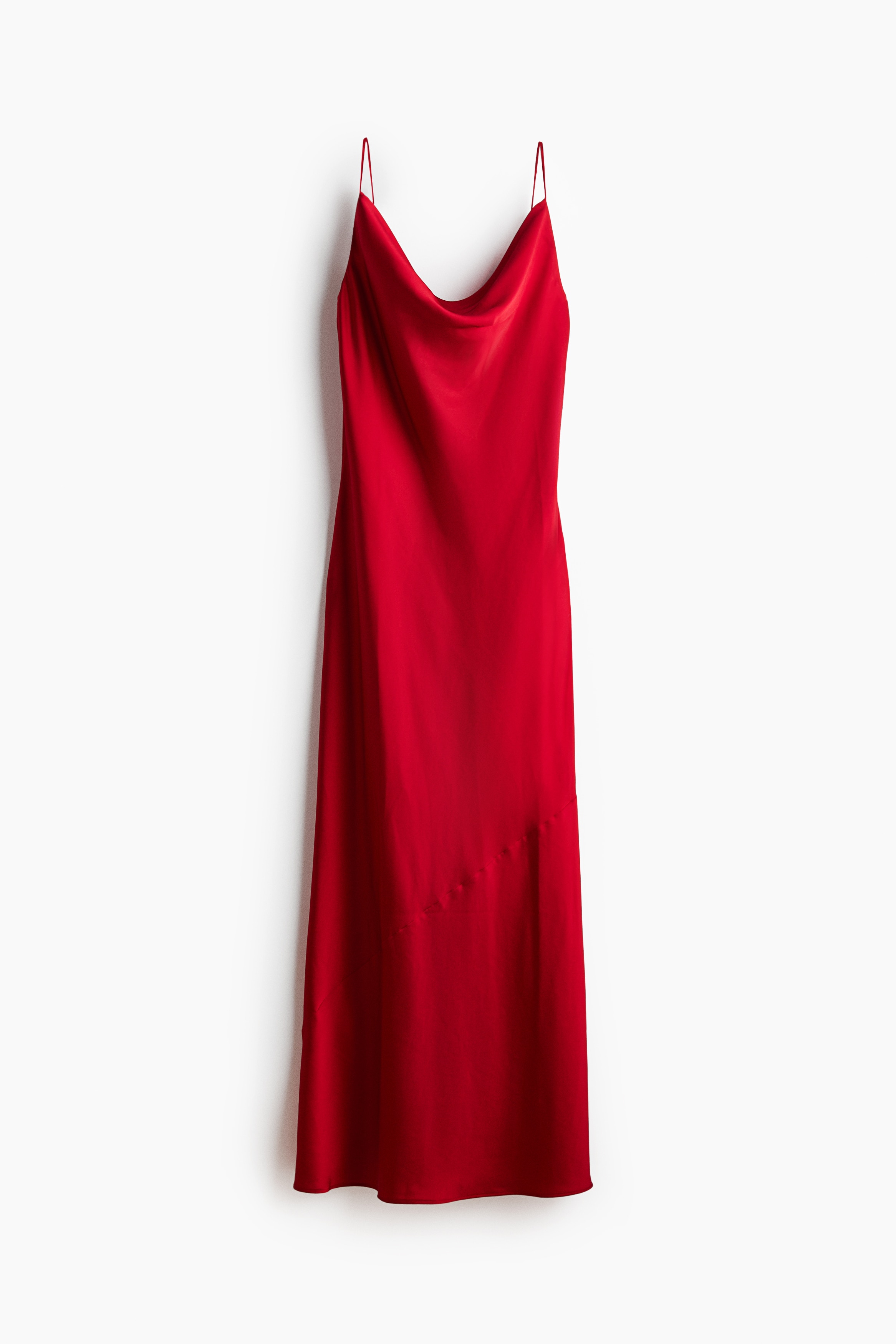 The model is wearing a red satin dress featuring a draped cowl neckline and thin spaghetti straps. The softly draped, fitted dress is styled with a gold-coloured cuff bracelet on the model's forearm.