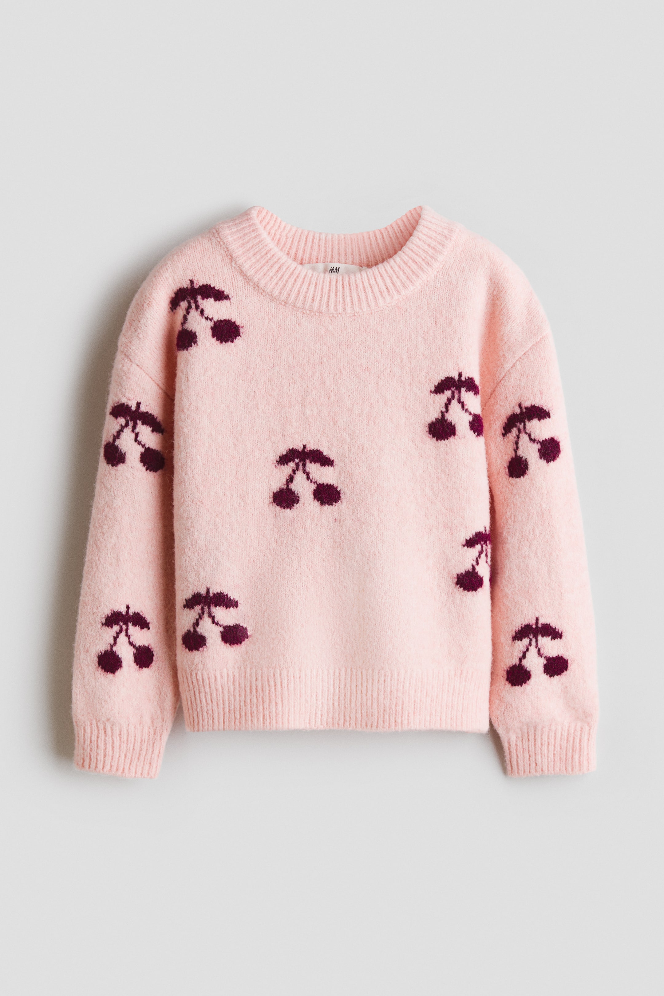 View larger image: A light pink fuzzy knit sweater featuring a repeating pattern of dark red cherries across the front. It is designed with a ribbed crew neck, ribbed cuffs, and a ribbed hem.