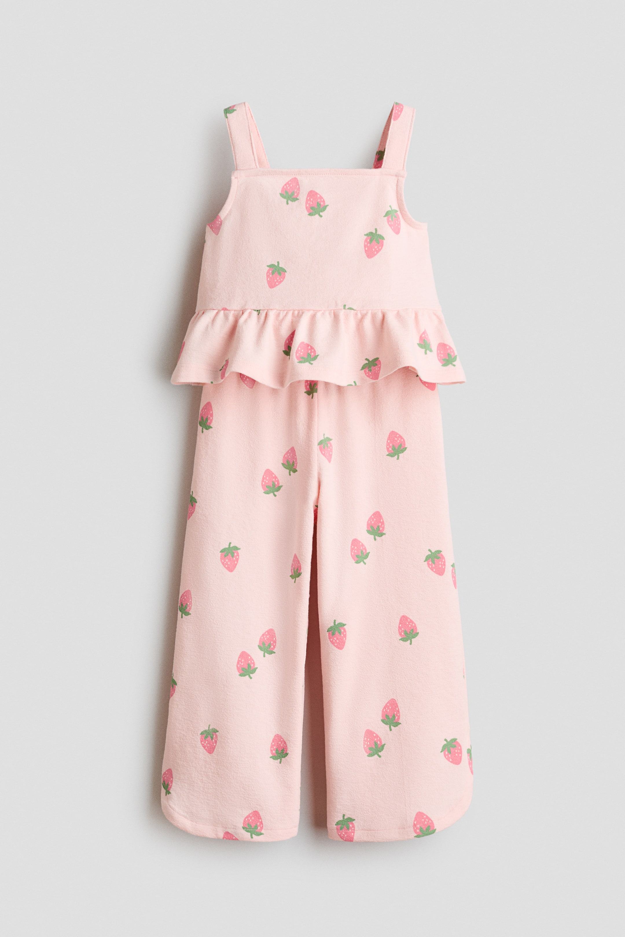 Ver imagen más grande: Un conjunto de jersey suave en color rosa muestra un top con tirantes y pantalones a juego, ambos con un estampado de fresas. El top está diseñado con un escote cuadrado y un volante peplum, y los pantalones presentan una cintura elástica y dobladillos curvados.