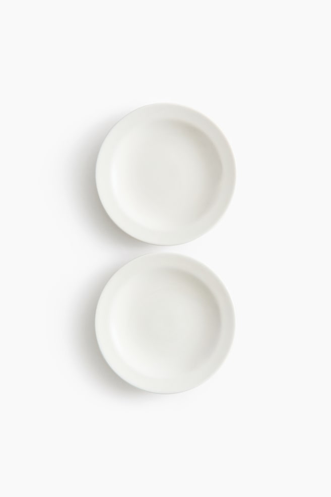 Two round, off-white plates are presented flat, facing upwards. Each plate is designed with a slightly raised rim and a smooth, flat centre. - 1