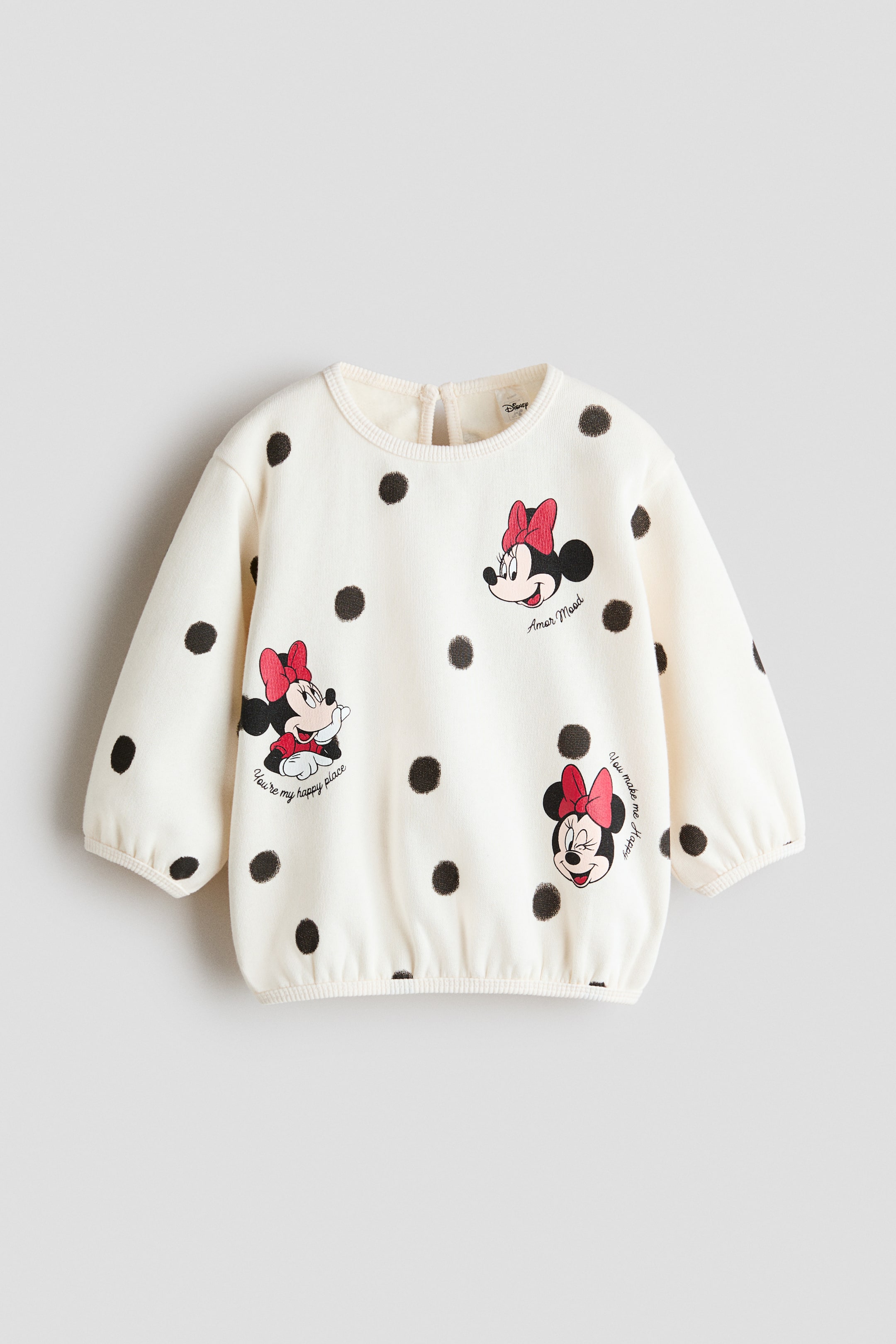Visualizza l'immagine ingrandita: Un maglione in pile color crema è mostrato frontalmente, caratterizzato da un motivo a pois neri e grafiche stampate di Minnie Mouse con testo in corsivo. Il capo mostra uno scollo tondo a costine con un’apertura a goccia sul retro visibile, spalle scese e maniche voluminose con polsini stretti a costine.