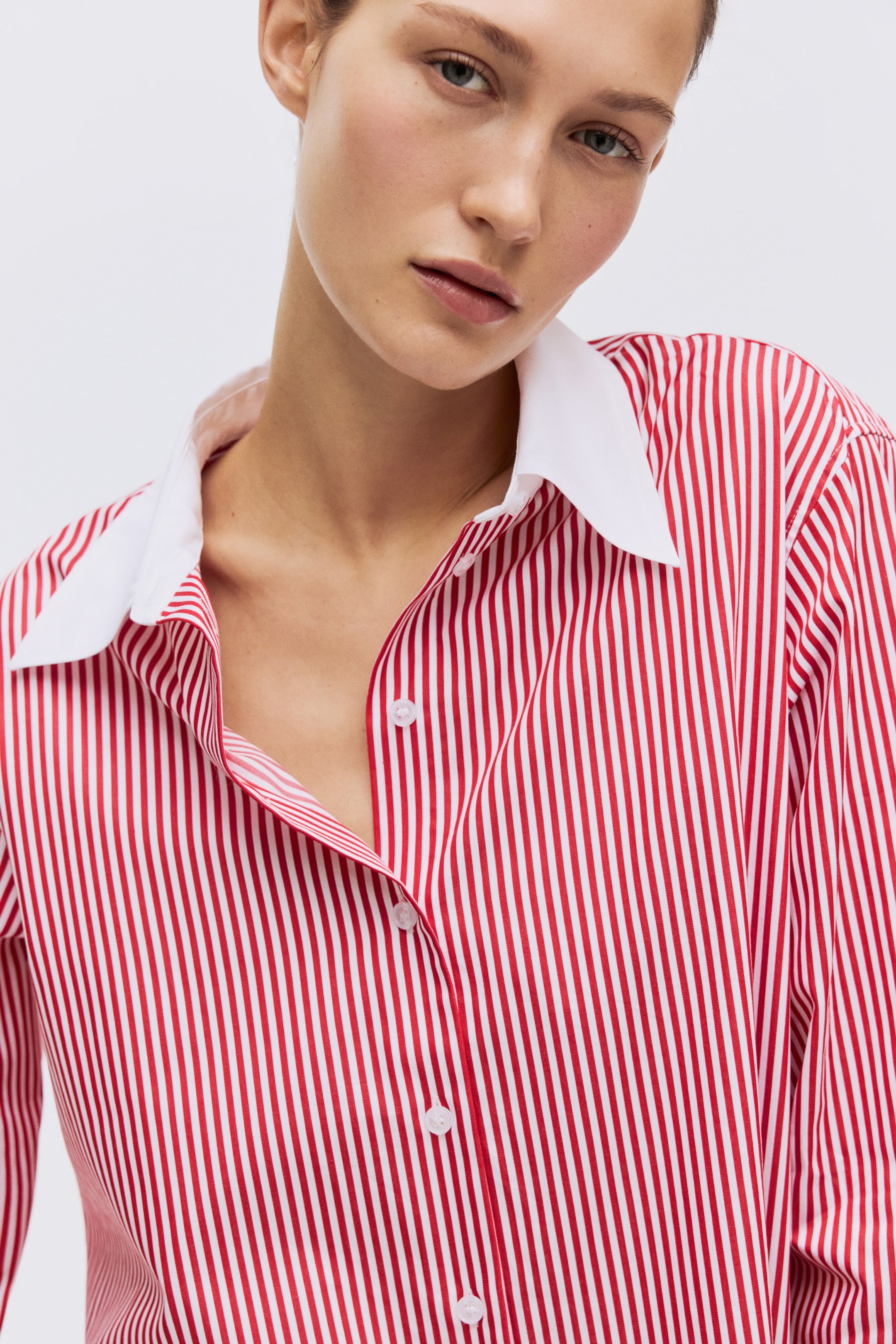 View larger image: A red-and-white striped shirt features a crisp white pointed collar and a front button placket. Several round white buttons are visible, with the top ones left unfastened to create an open neckline.