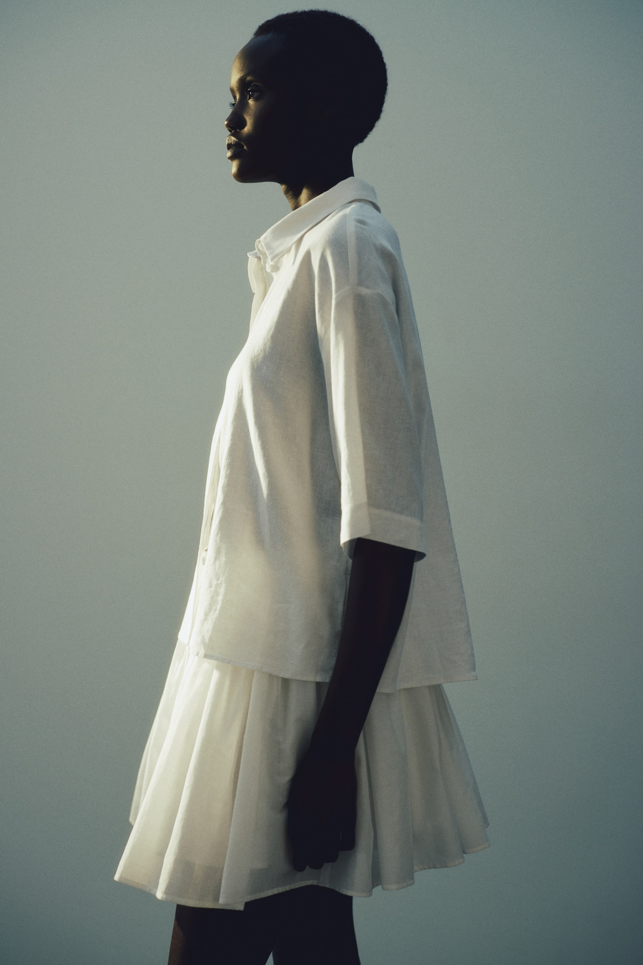 View larger image: The model wears a white linen-and-viscose blend shirt with an airy weave. The shirt features a collar, front buttons, gently dropped shoulders and elbow-length sleeves, and is layered over a white tiered skirt.