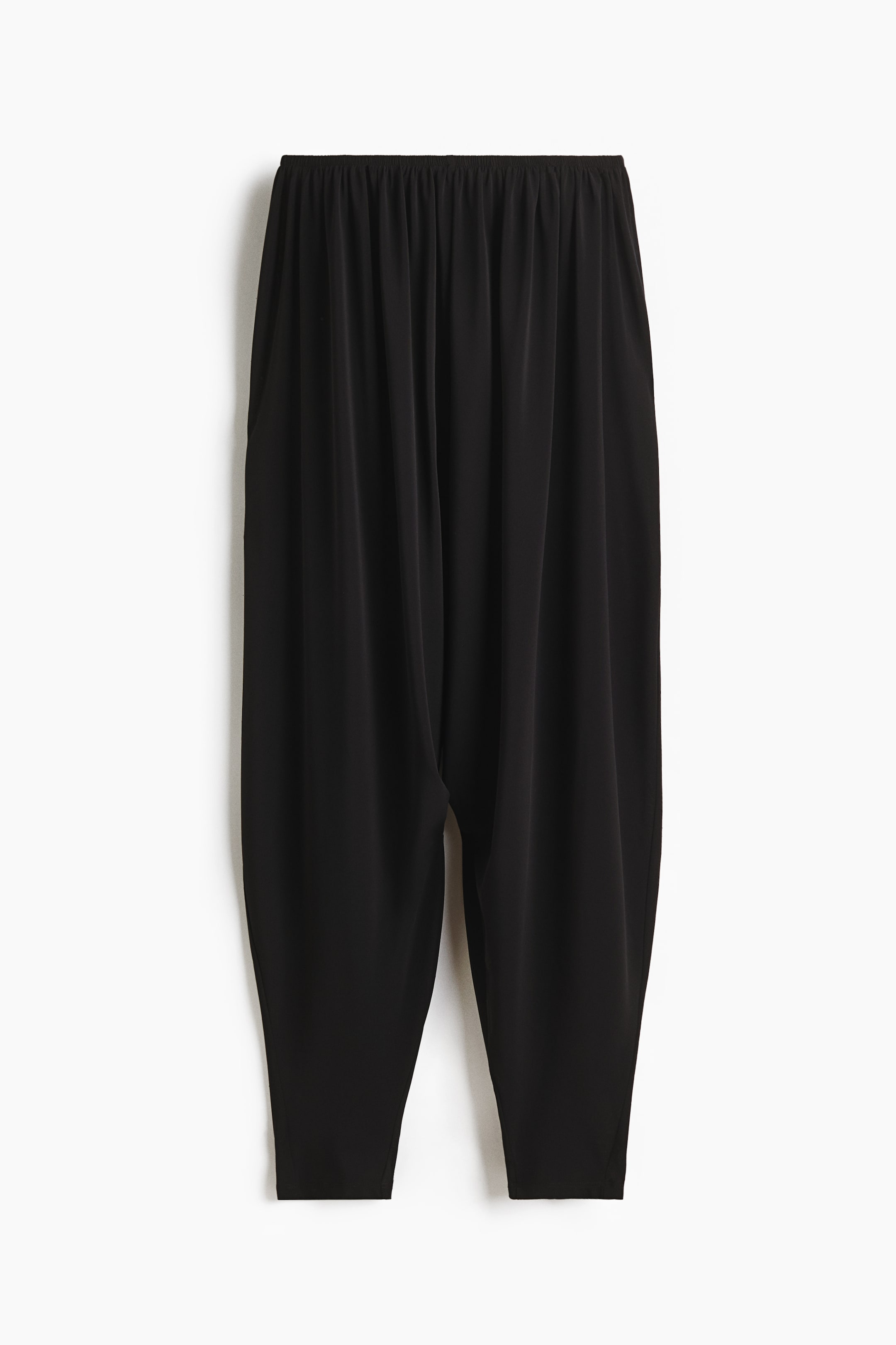View larger image: Black trousers are shown from the front, featuring an elastic, gathered waist. They are designed with a loose, flowing fit through the legs, tapering slightly towards the ankles.